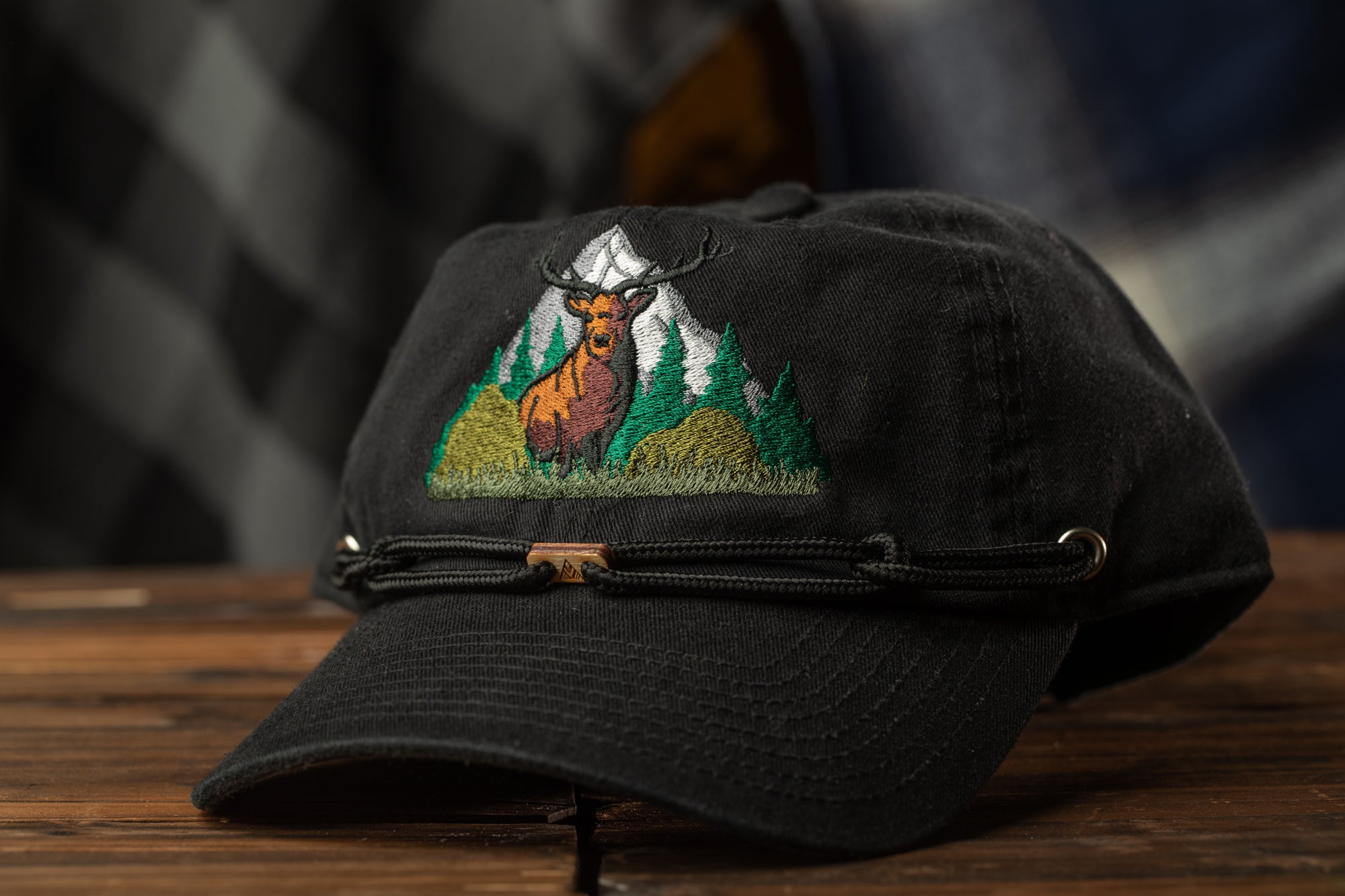 A black baseball cap with a deer embroidered on the front, sitting on a wooden surface.