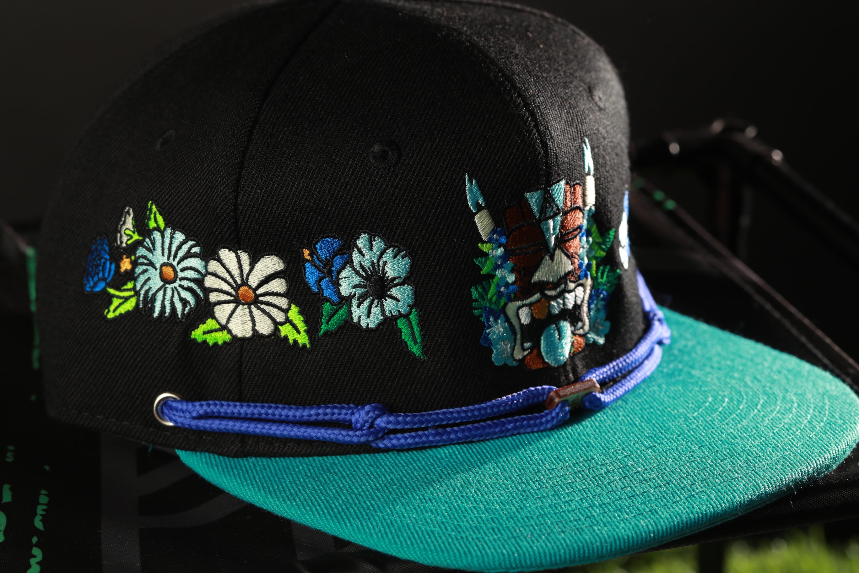 A black baseball cap with colorful floral embroidery and a blue brim.