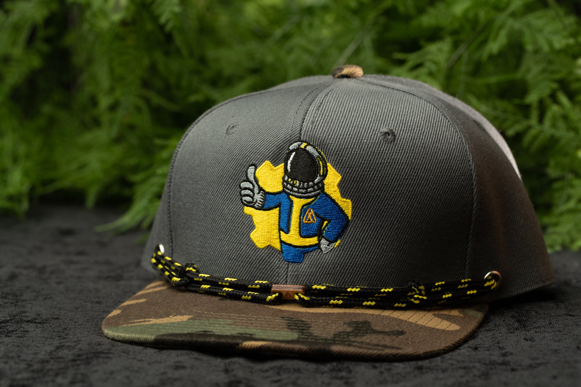 A gray baseball cap with a yellow and blue embroidered design of a person wearing a blue and yellow outfit, giving the impression of a character from a video game.
