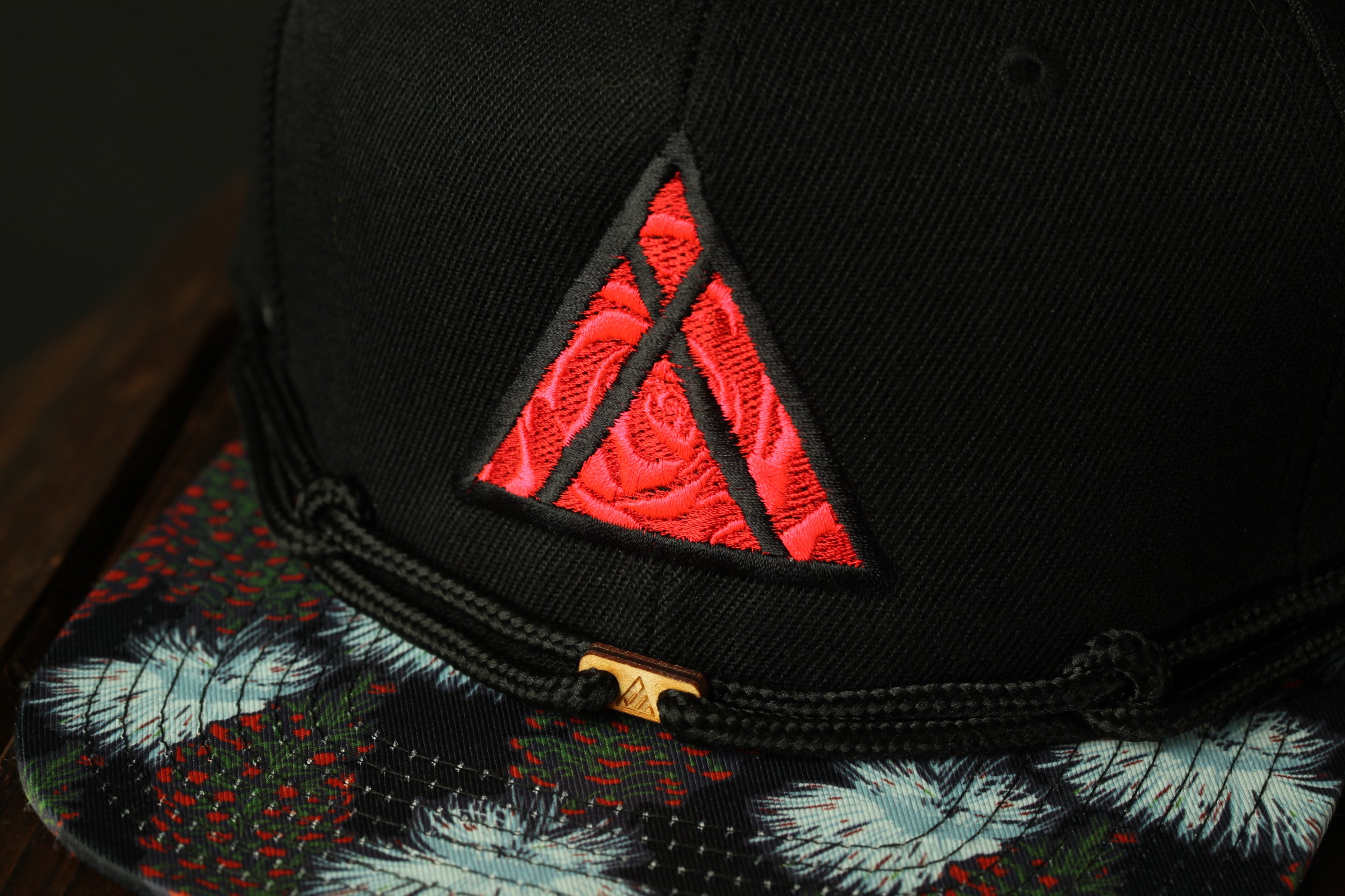 A close-up view of a black baseball cap with a red triangle embroidered on the front.