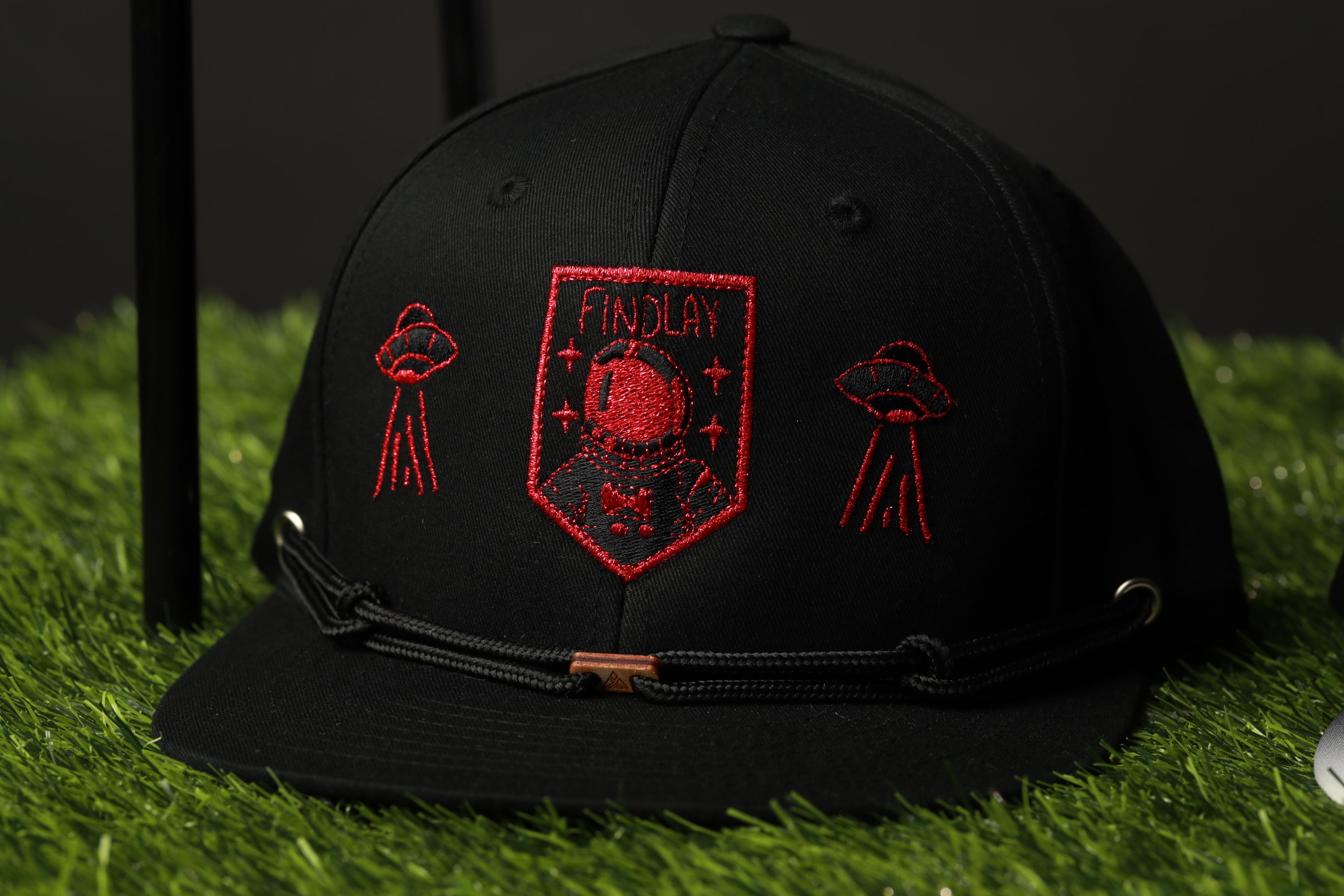 A black baseball cap with red embroidered designs on it, including a shield-shaped design with a red border and the word "FINDlay" written on it.