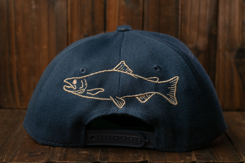 A navy blue baseball cap with a fish embroidered on the front, sitting on a wooden surface.
