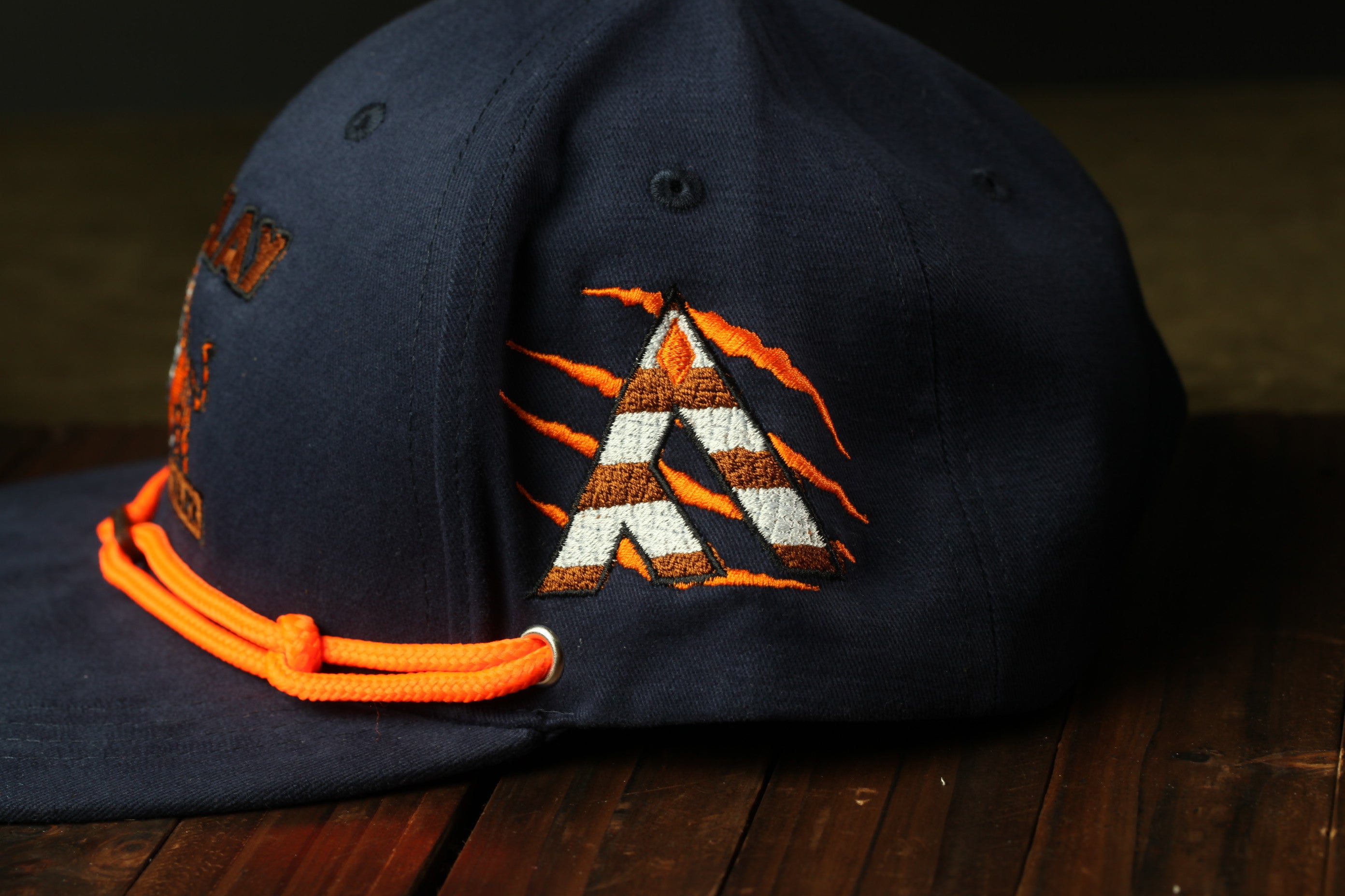 A navy blue baseball cap with an orange and white striped logo on the side, sitting on a wooden surface.