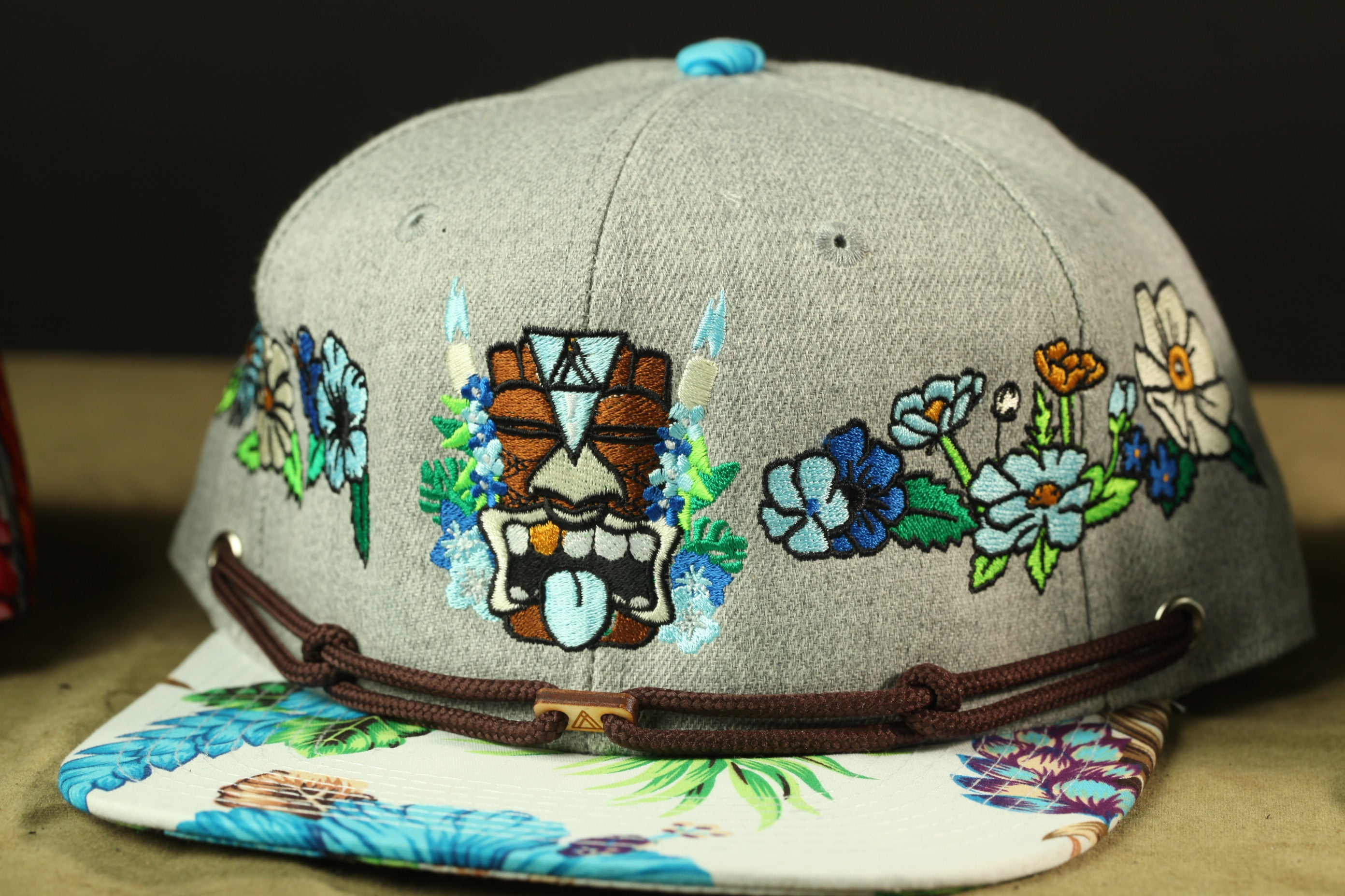 A gray baseball cap with colorful floral embroidery and a tiki mask design.