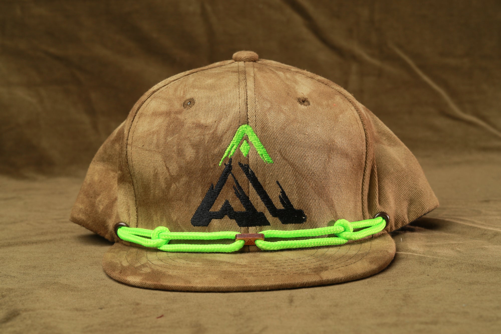 A brown baseball cap with a green rope strap and a black logo on the front.