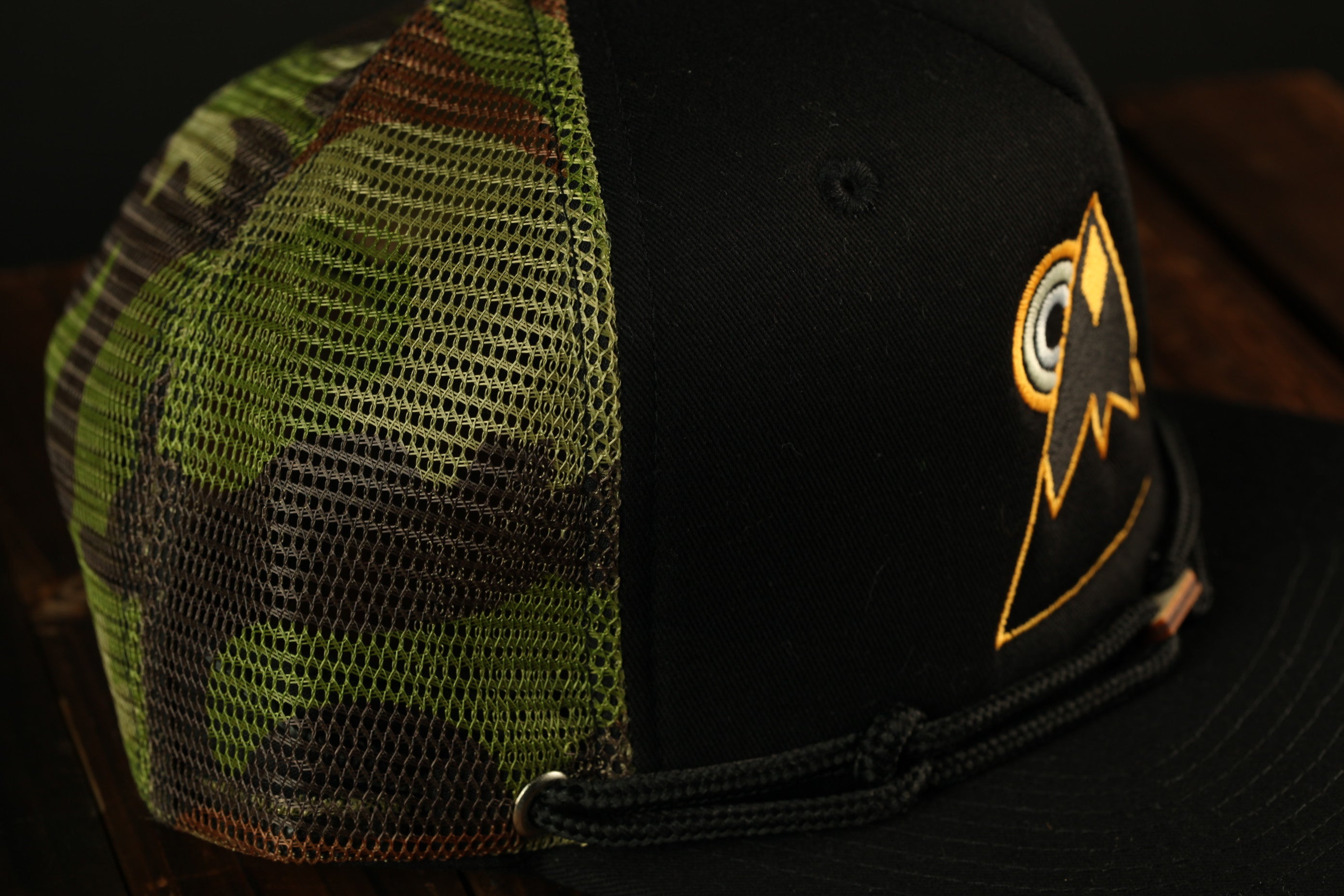 A close-up view of a black baseball cap with a mesh pattern on the side and a logo on the front.