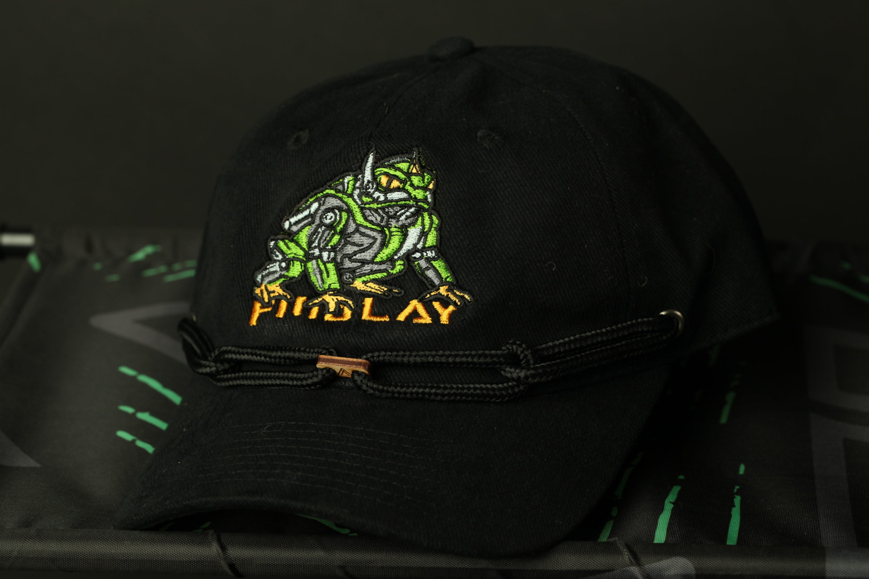 A black baseball cap with a green and yellow design on the front, featuring a cartoon-like creature.