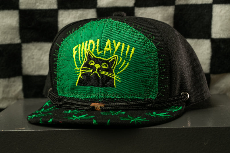 A black baseball cap with a green and yellow embroidered design on the front, featuring a cat's face and the text "FINOLAY!!".
