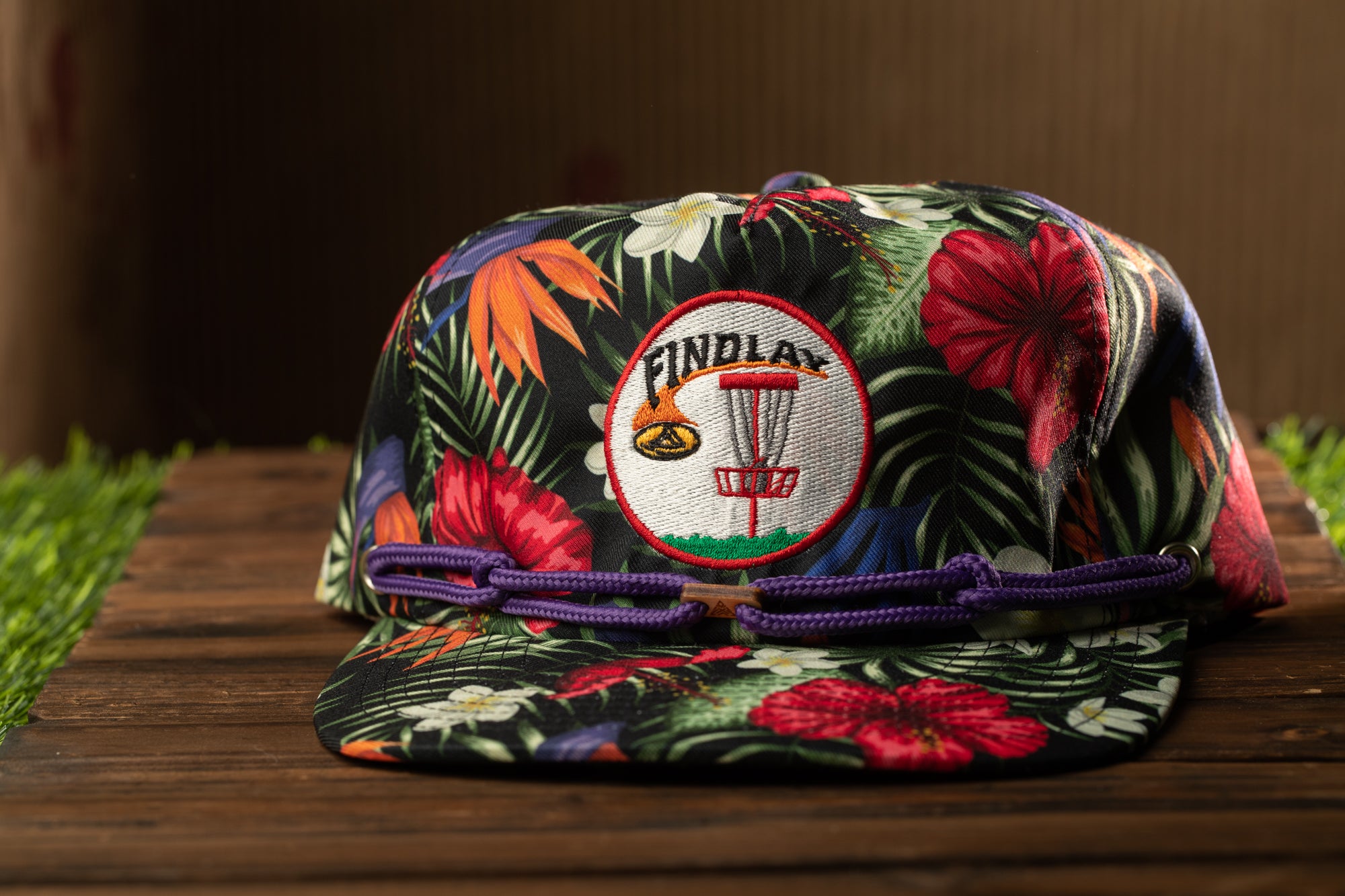 A colorful floral cap with a frisbee design and the word "FINDlay" on it, placed on a wooden surface.
