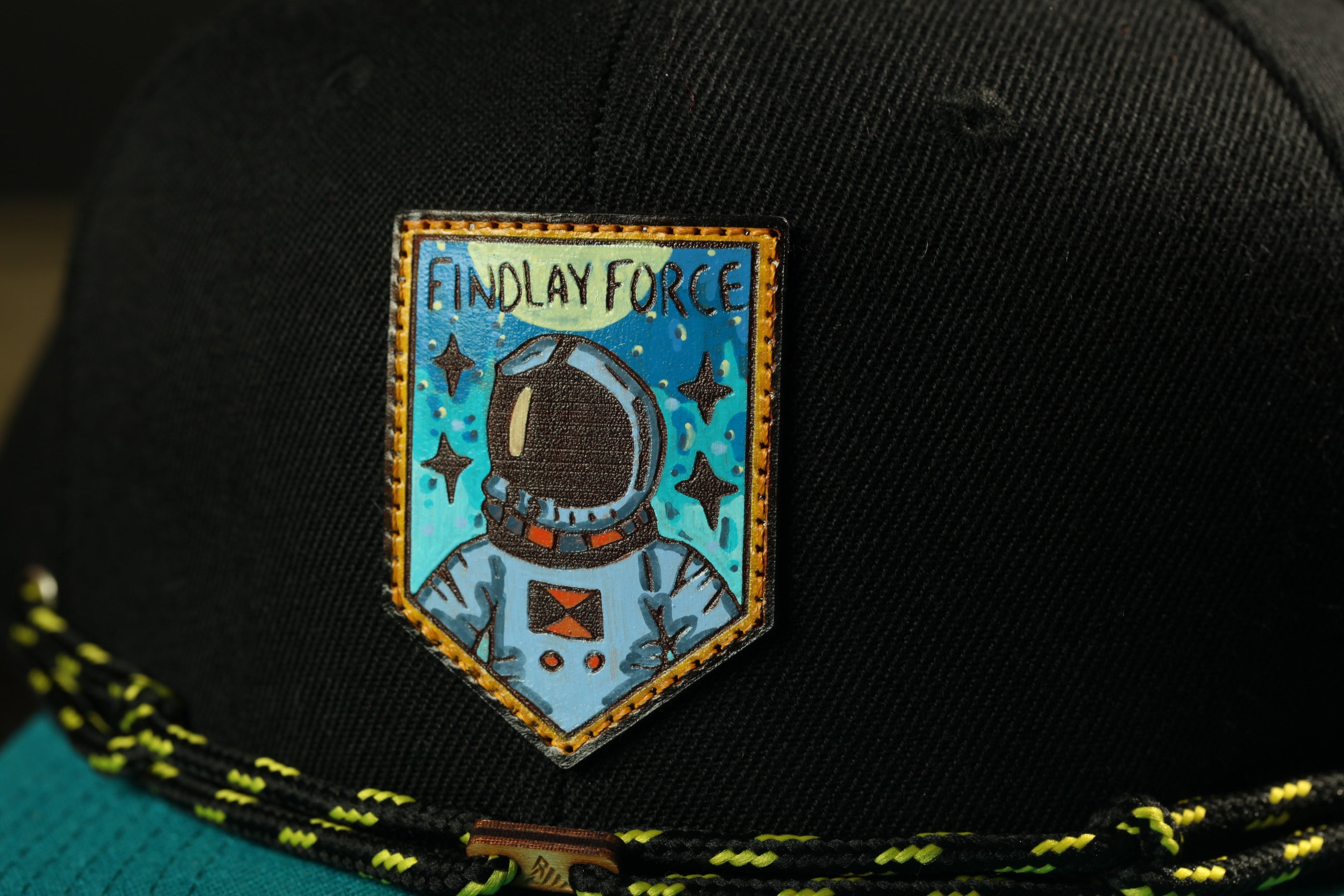 A close-up of a black baseball cap with a patch featuring an astronaut and the text "Findlay Force" printed on it.