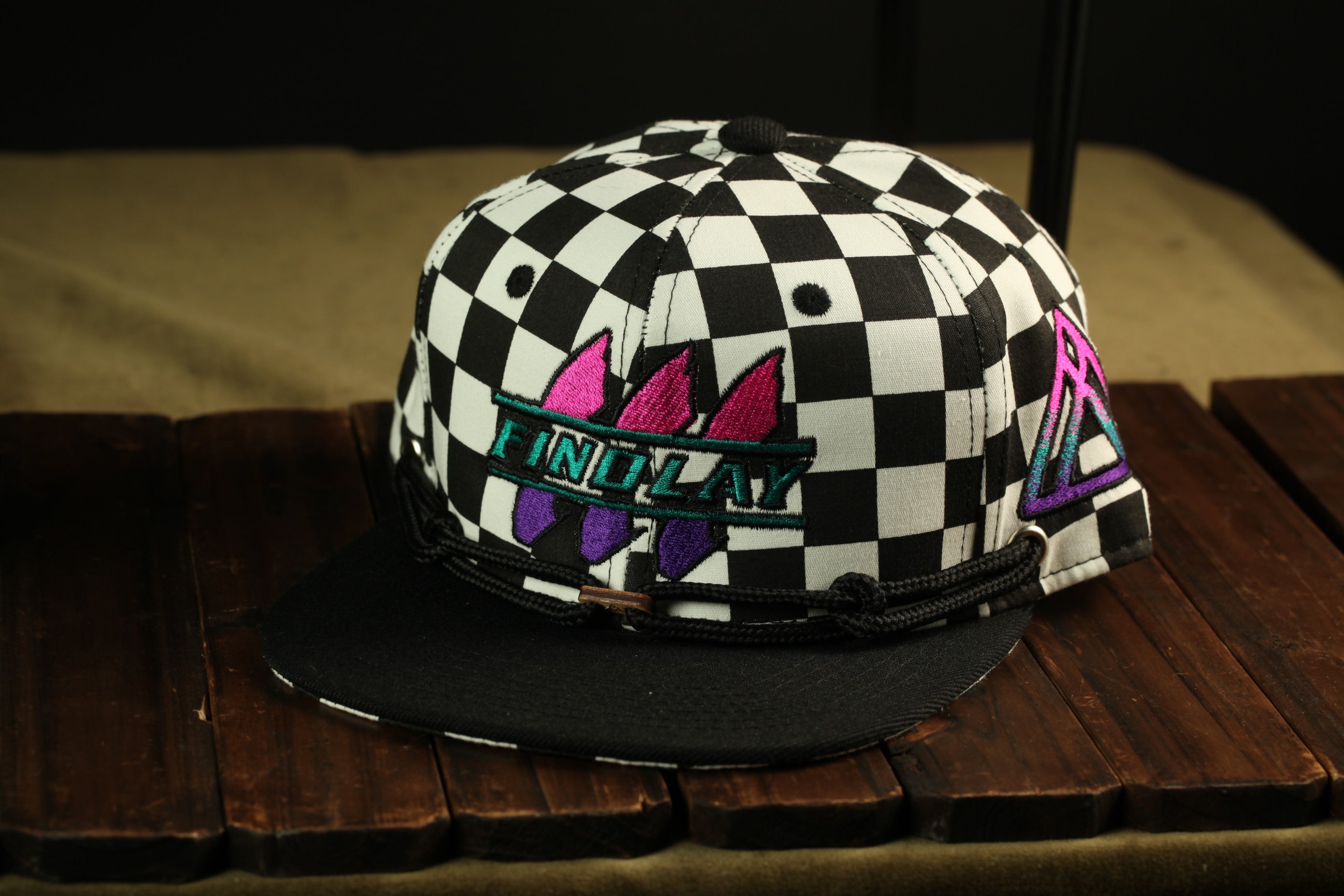 A black and white checkered baseball cap with a graphic design on it, sitting on a wooden surface.