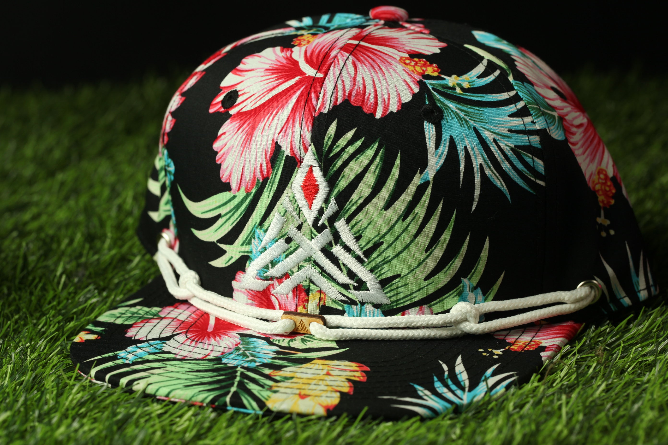 A colorful floral baseball cap with a white lace trim, resting on a grassy surface.