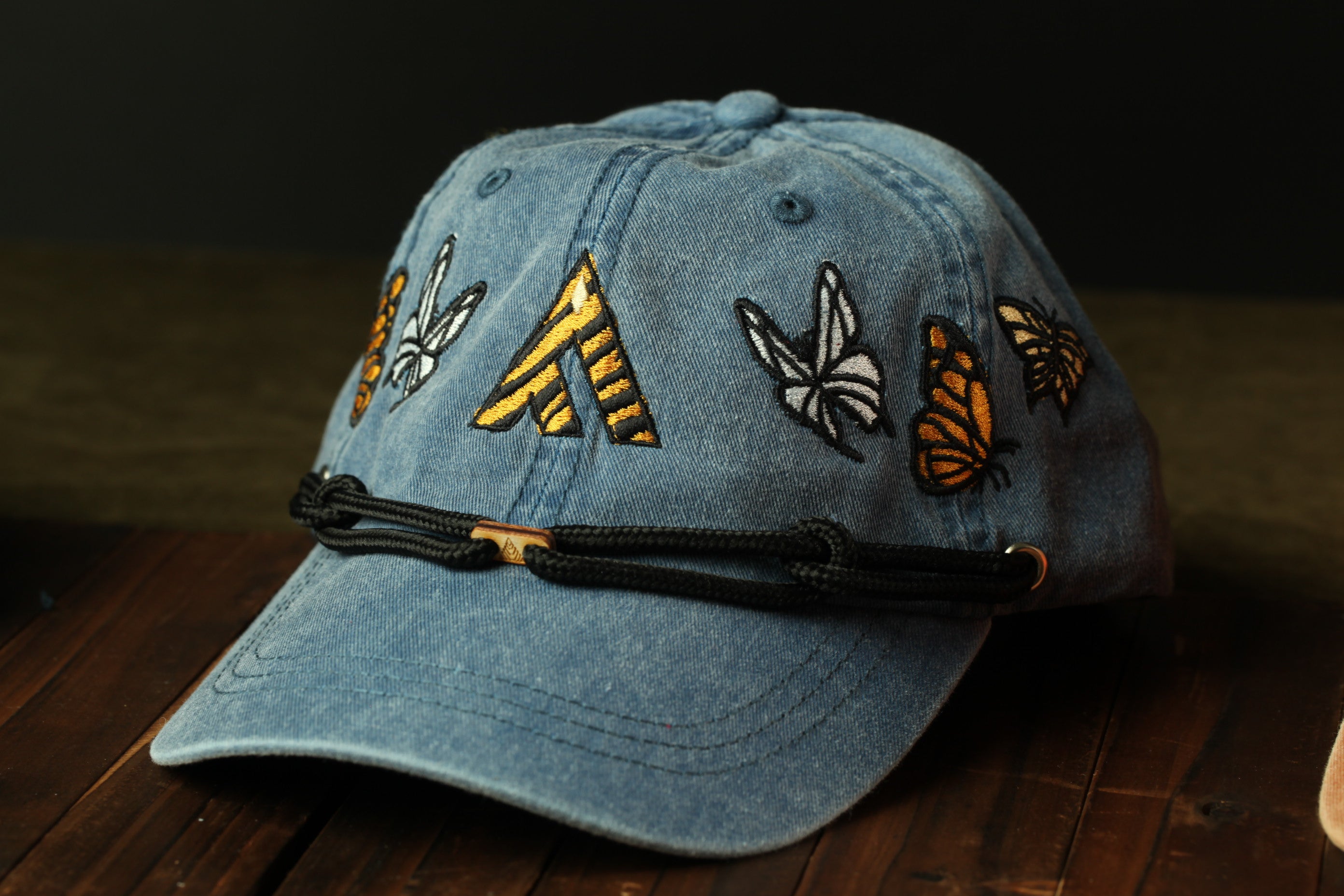A blue denim baseball cap with yellow and orange butterfly designs on the front.