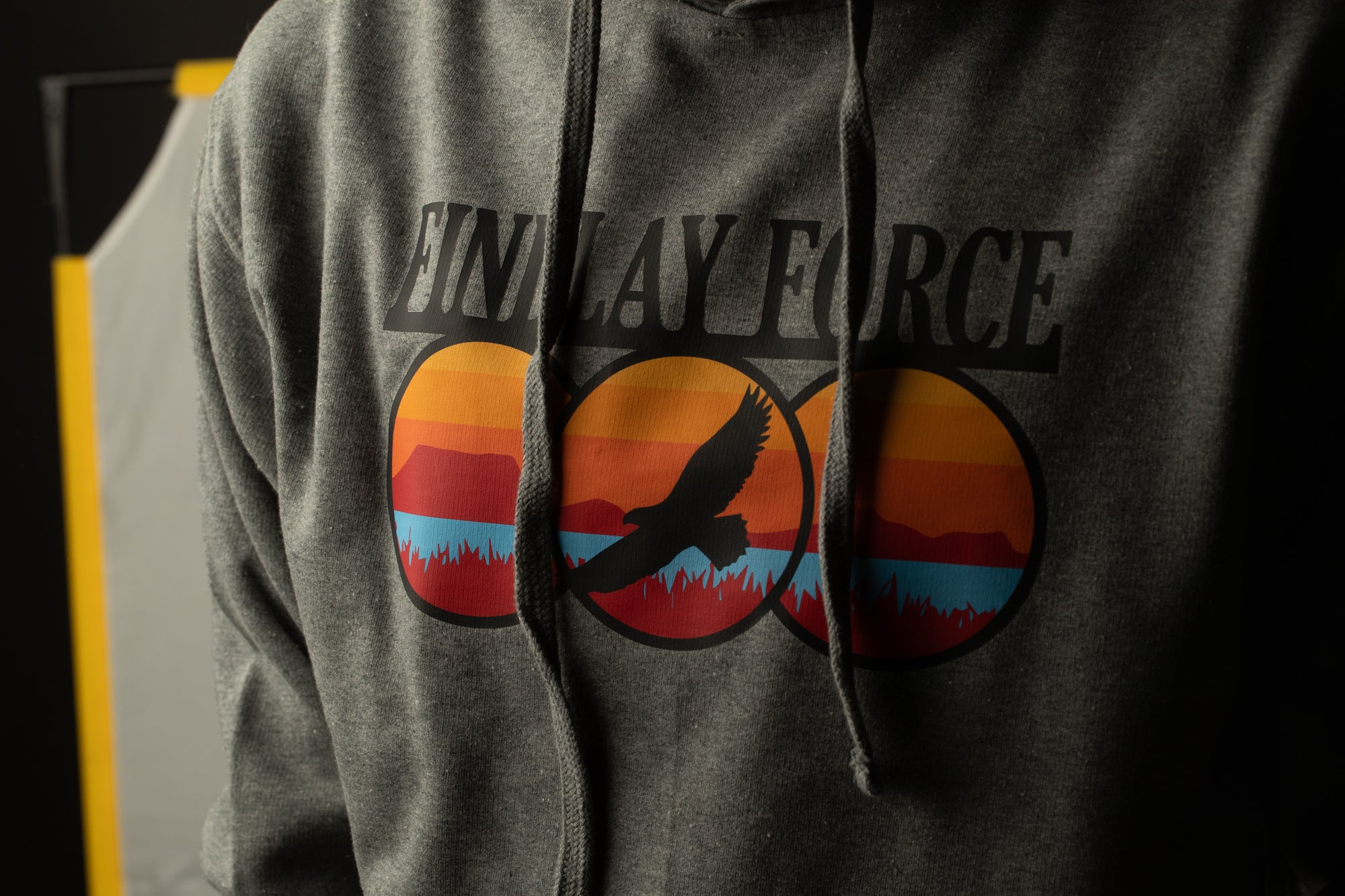 A person wearing a grey hoodie with a graphic design featuring a bird in flight and a sunset landscape.