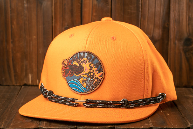 An orange baseball cap with a circular patch featuring a wave design and the word "IND" on it, placed on a wooden surface.
