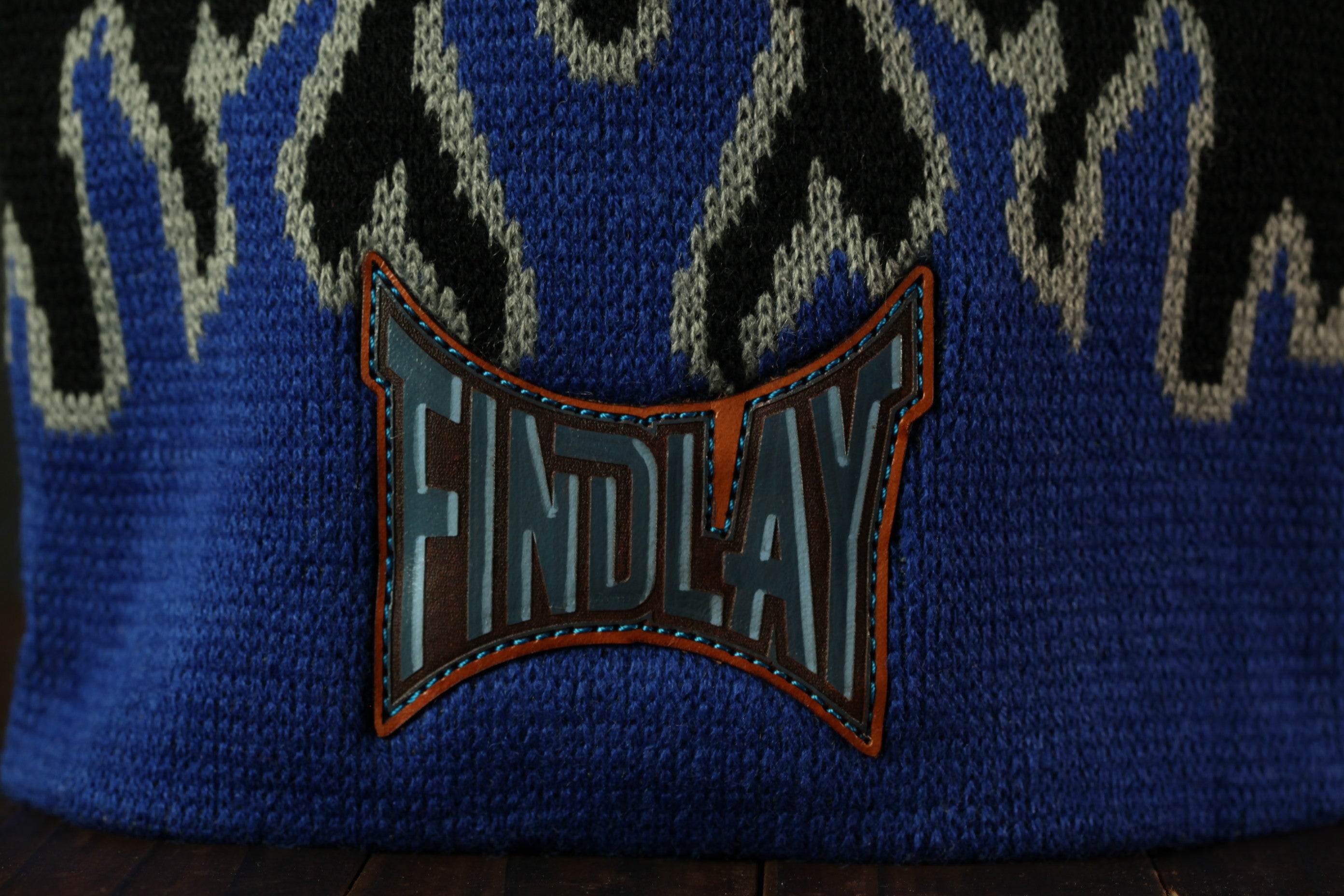 A close-up view of a blue and black knitted or crocheted hat with a large, bold, and stylized logo or text on the front.