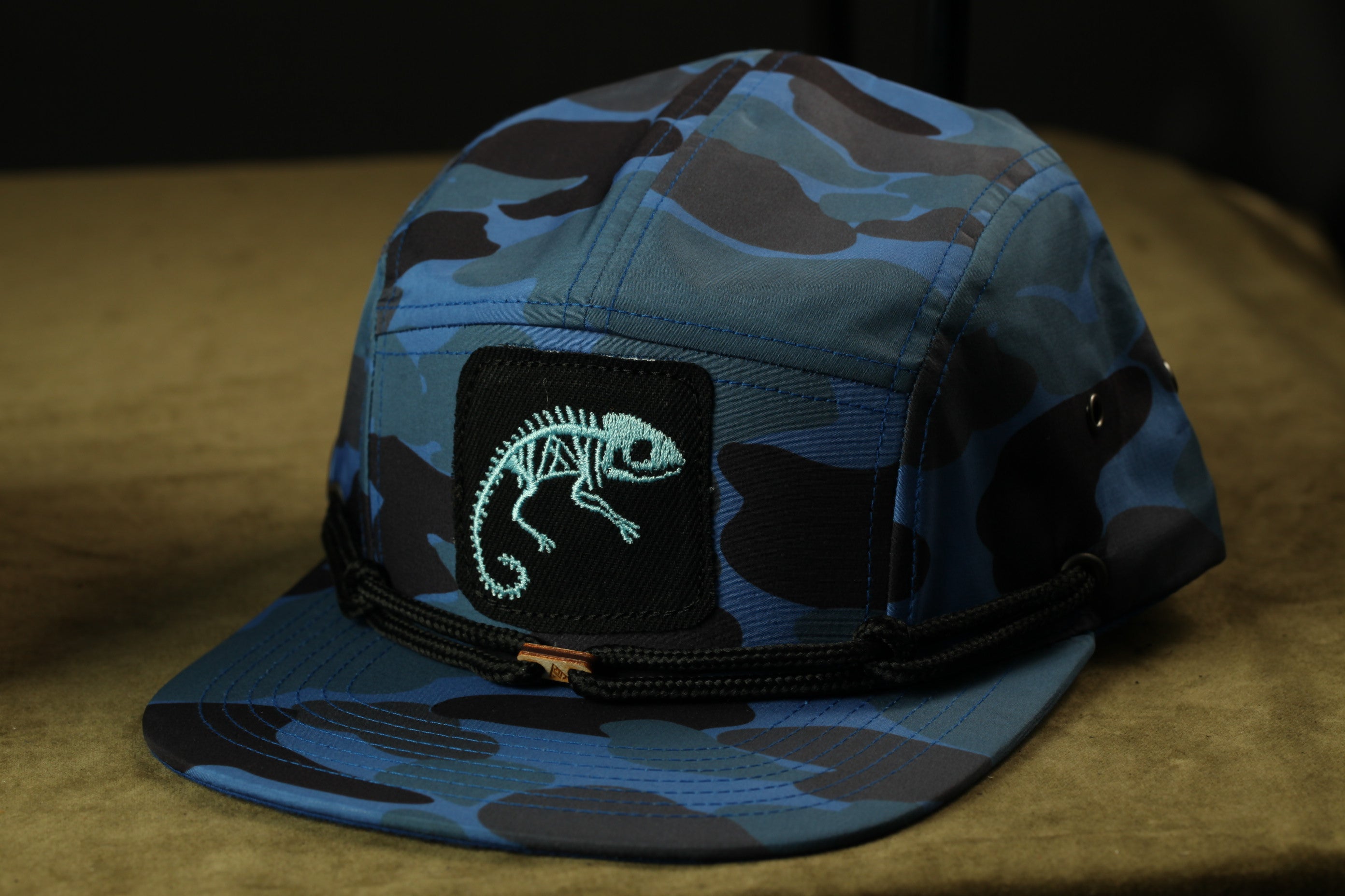 A camouflage baseball cap with a chameleon design on the front.