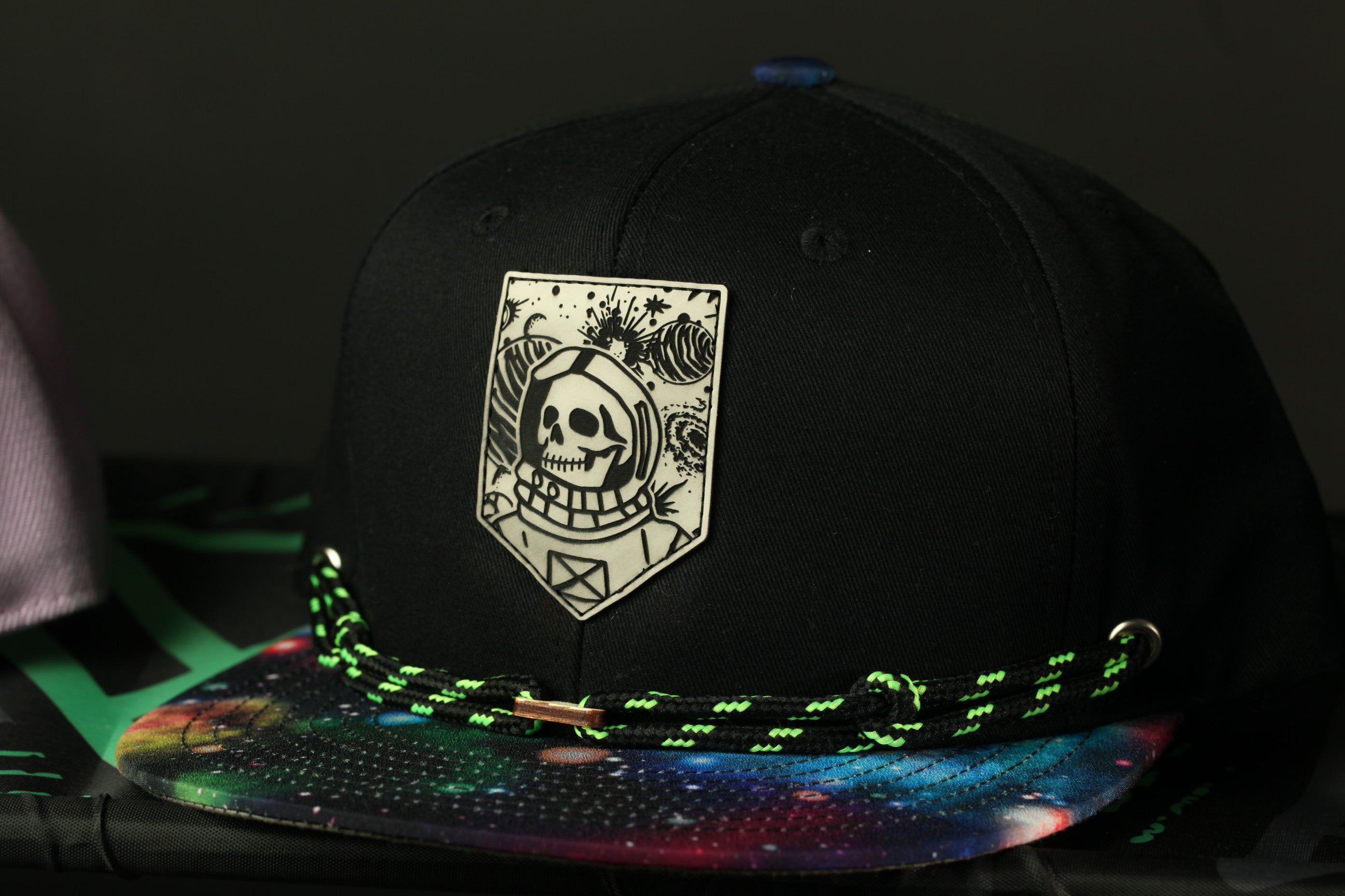 A black baseball cap with a skull and space-themed design on the front, and a colorful, space-themed brim.