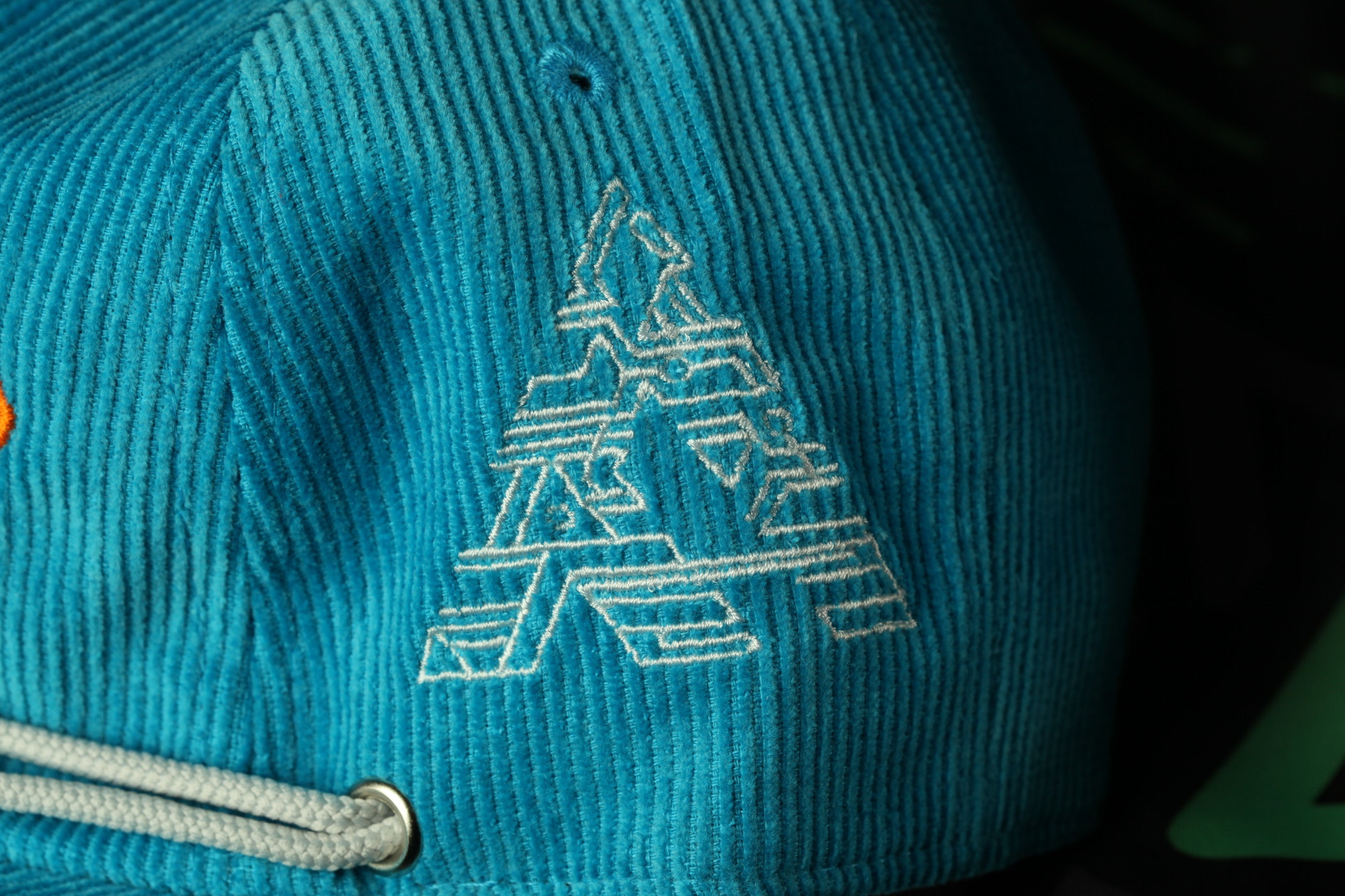 A close-up view of a teal-colored baseball cap with a white geometric pattern or logo on the front.