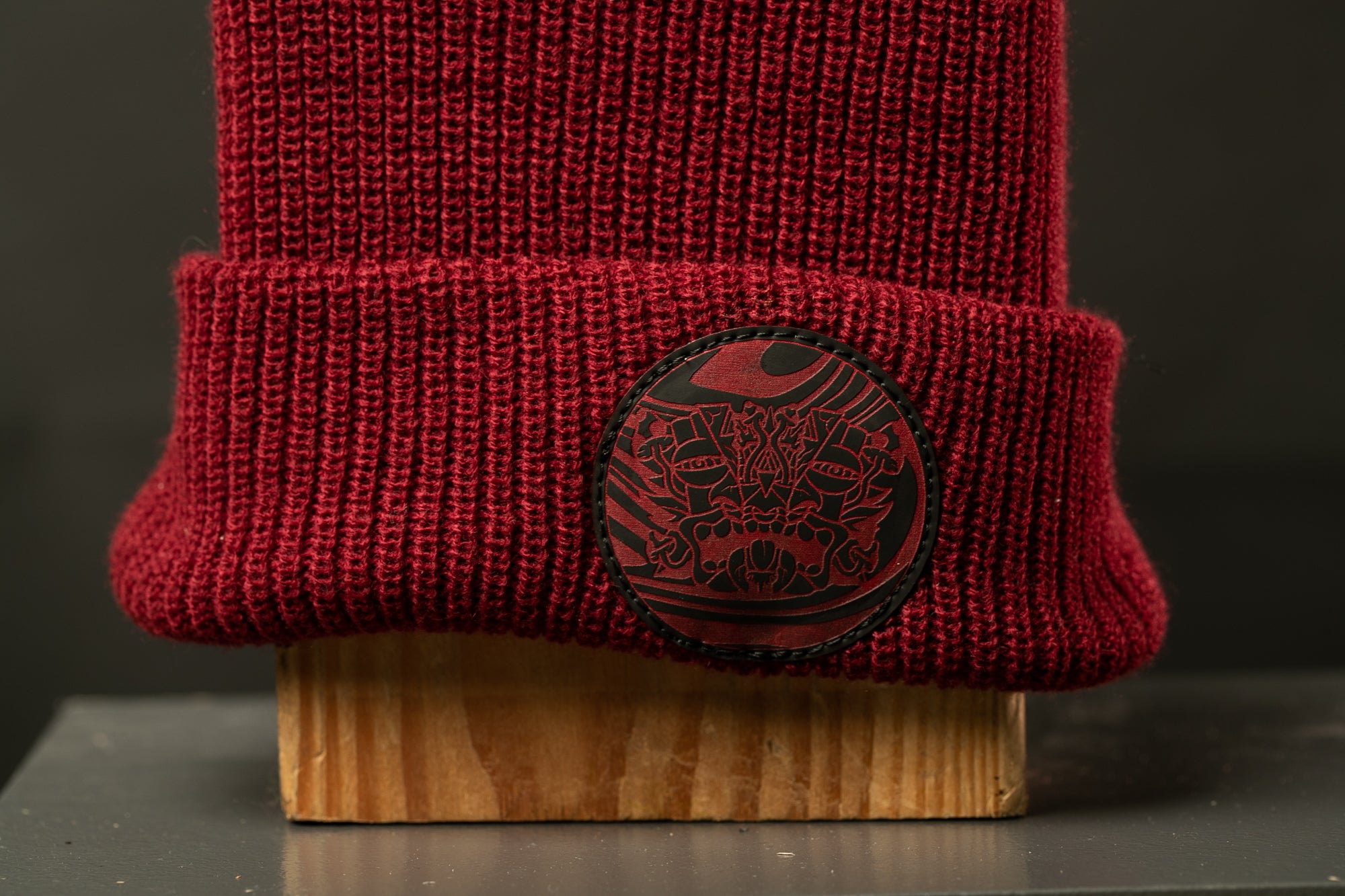 A close-up image of a red knit beanie with a circular black and red design on the front.