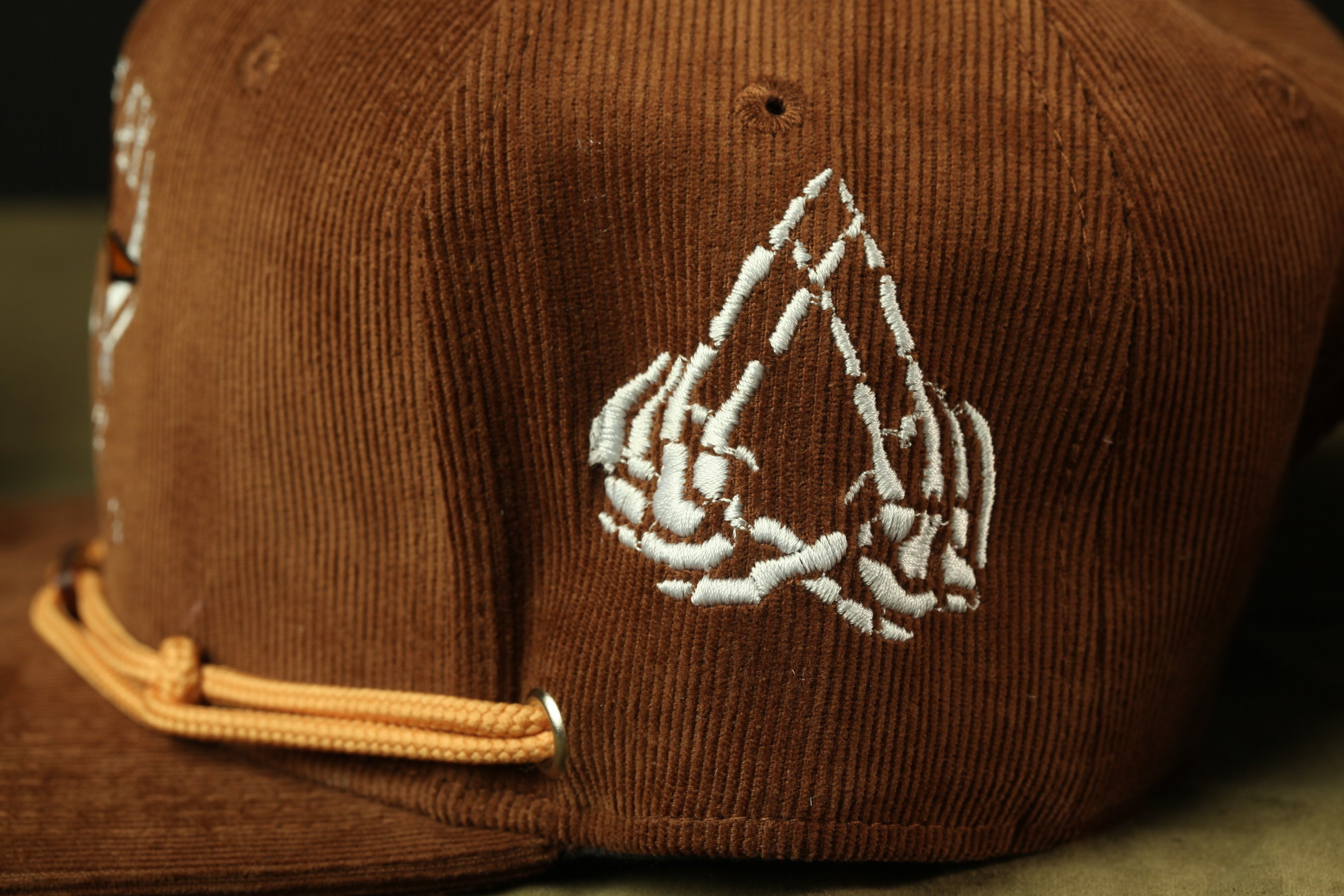 A close-up view of a brown baseball cap with a white embroidered design on the side.