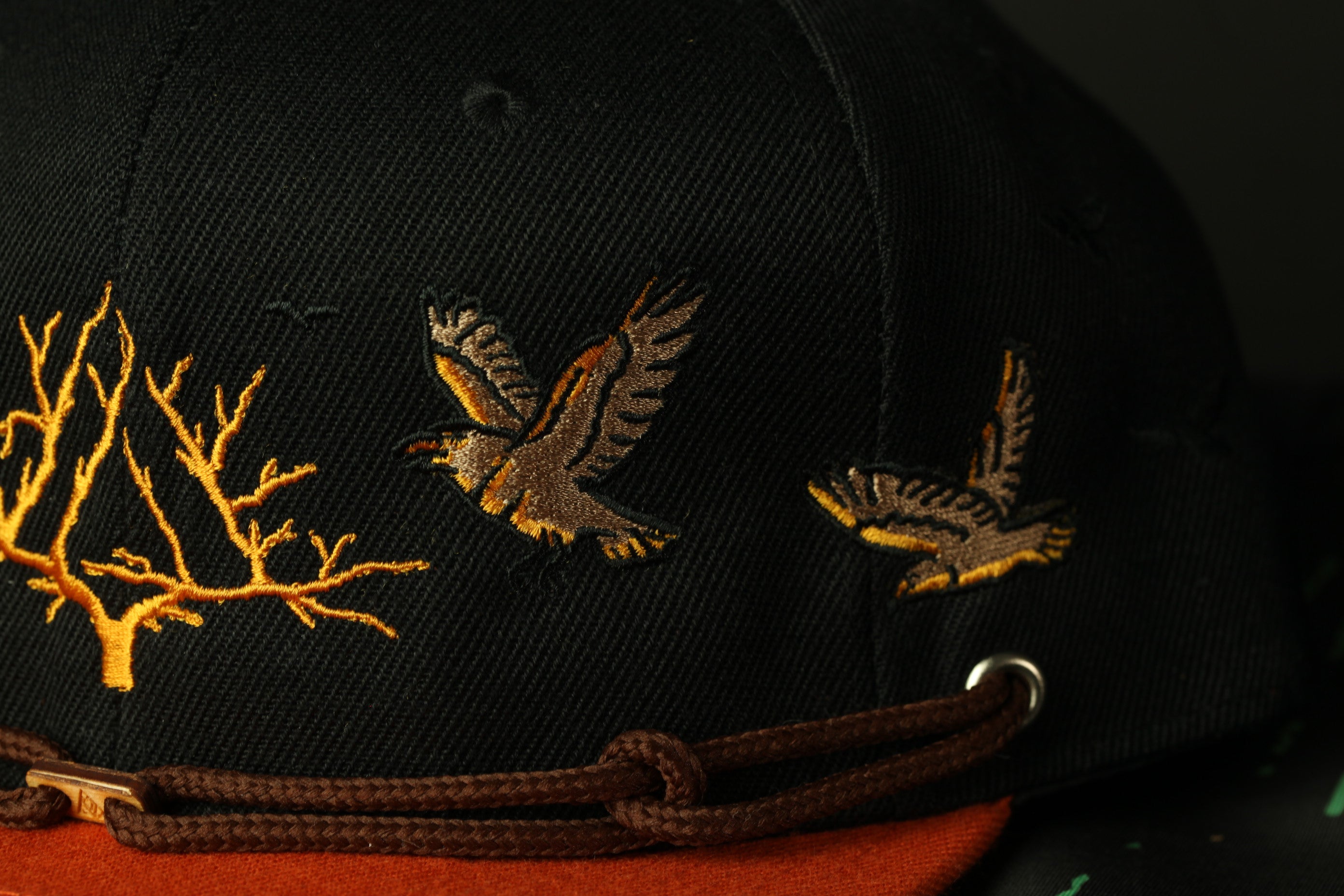 A close-up view of a black baseball cap with gold embroidered designs, including two birds in flight.