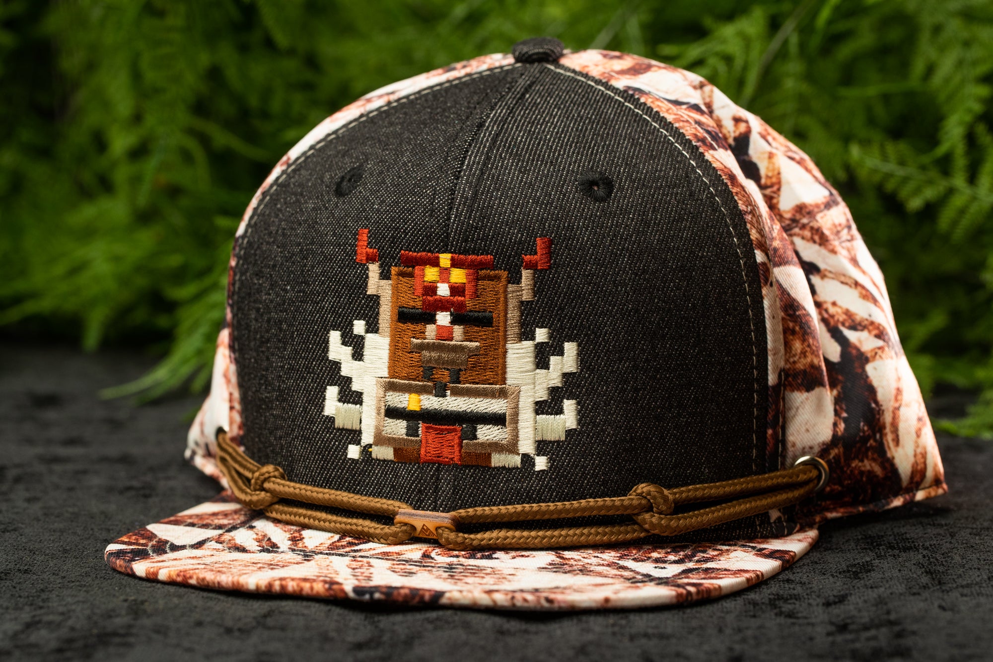 A black baseball cap with a colorful, pixelated design on the front, featuring a character or robot-like figure.