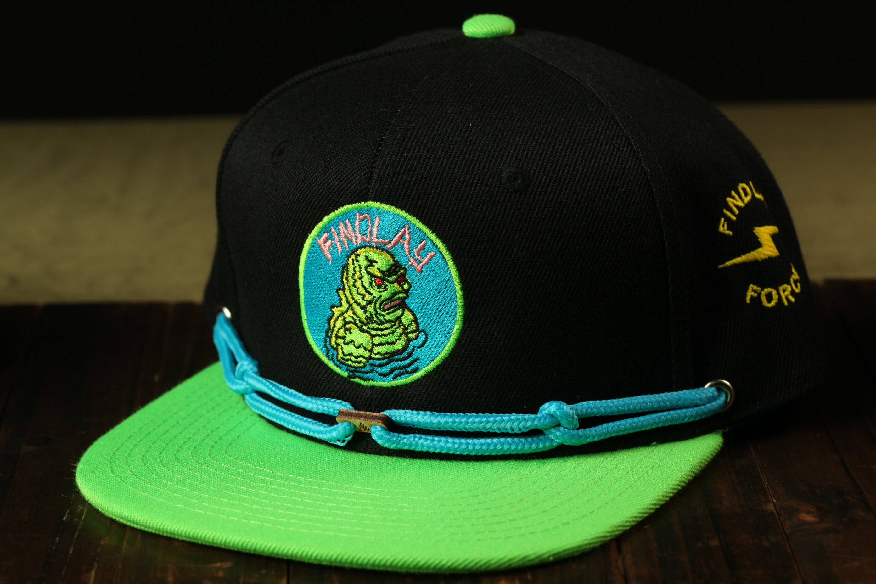 A black baseball cap with a green brim and a blue and green embroidered logo on the front.