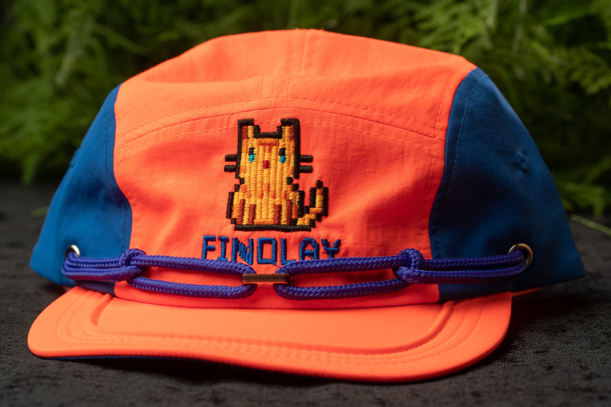 An orange and blue baseball cap with a pixelated cat design and the word "FINOLAY" printed on it.