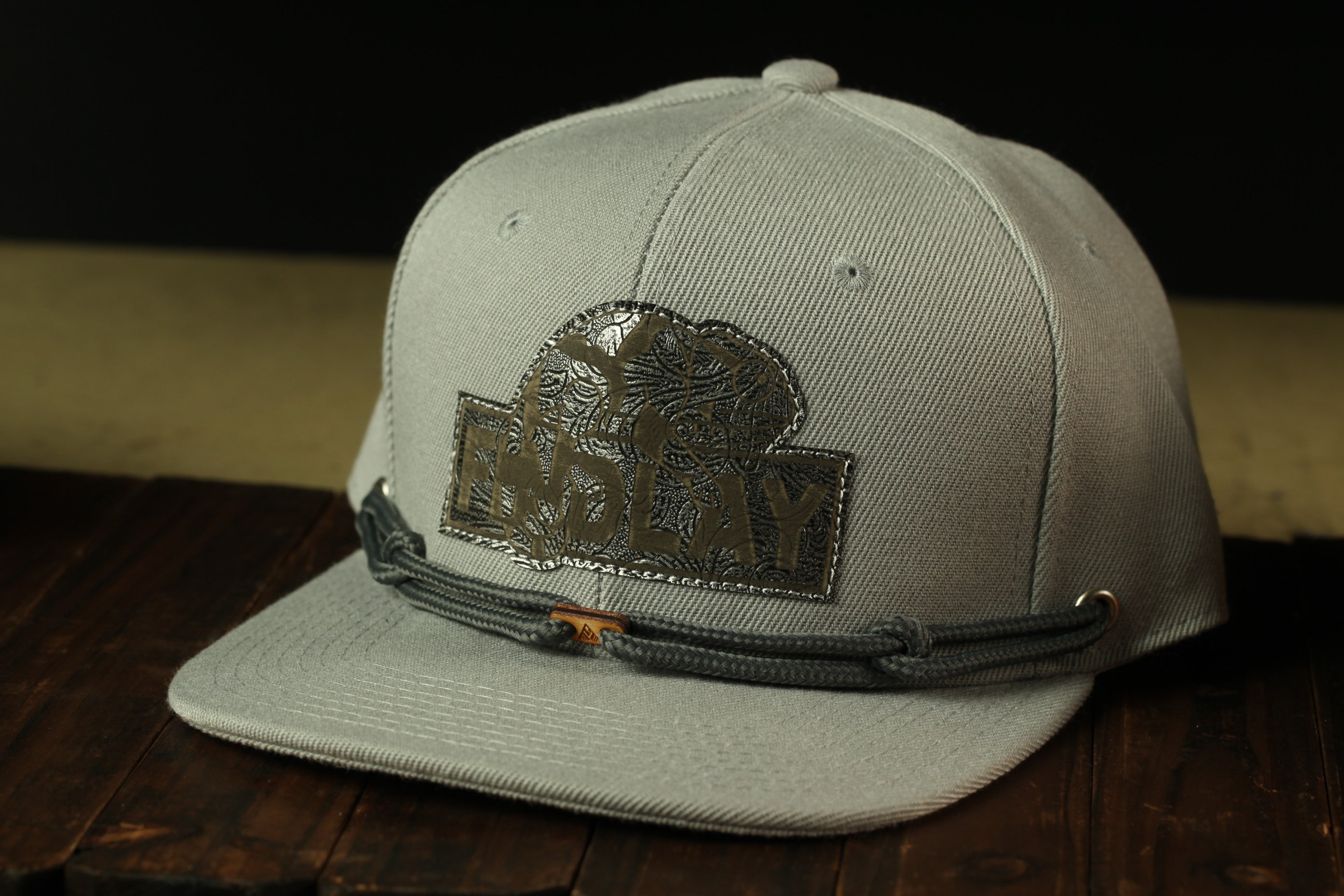A gray baseball cap with a black logo on the front, sitting on a wooden surface.