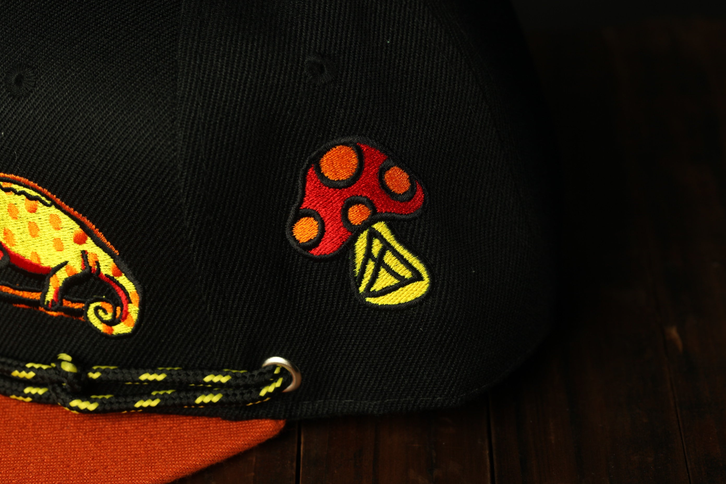 a close-up view of a black baseball cap with a colorful mushroom embroidered on it.