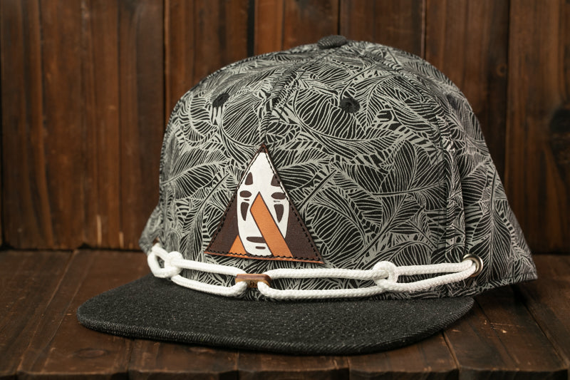 A black and white patterned baseball cap with a triangular patch featuring a face design, resting on a wooden surface.