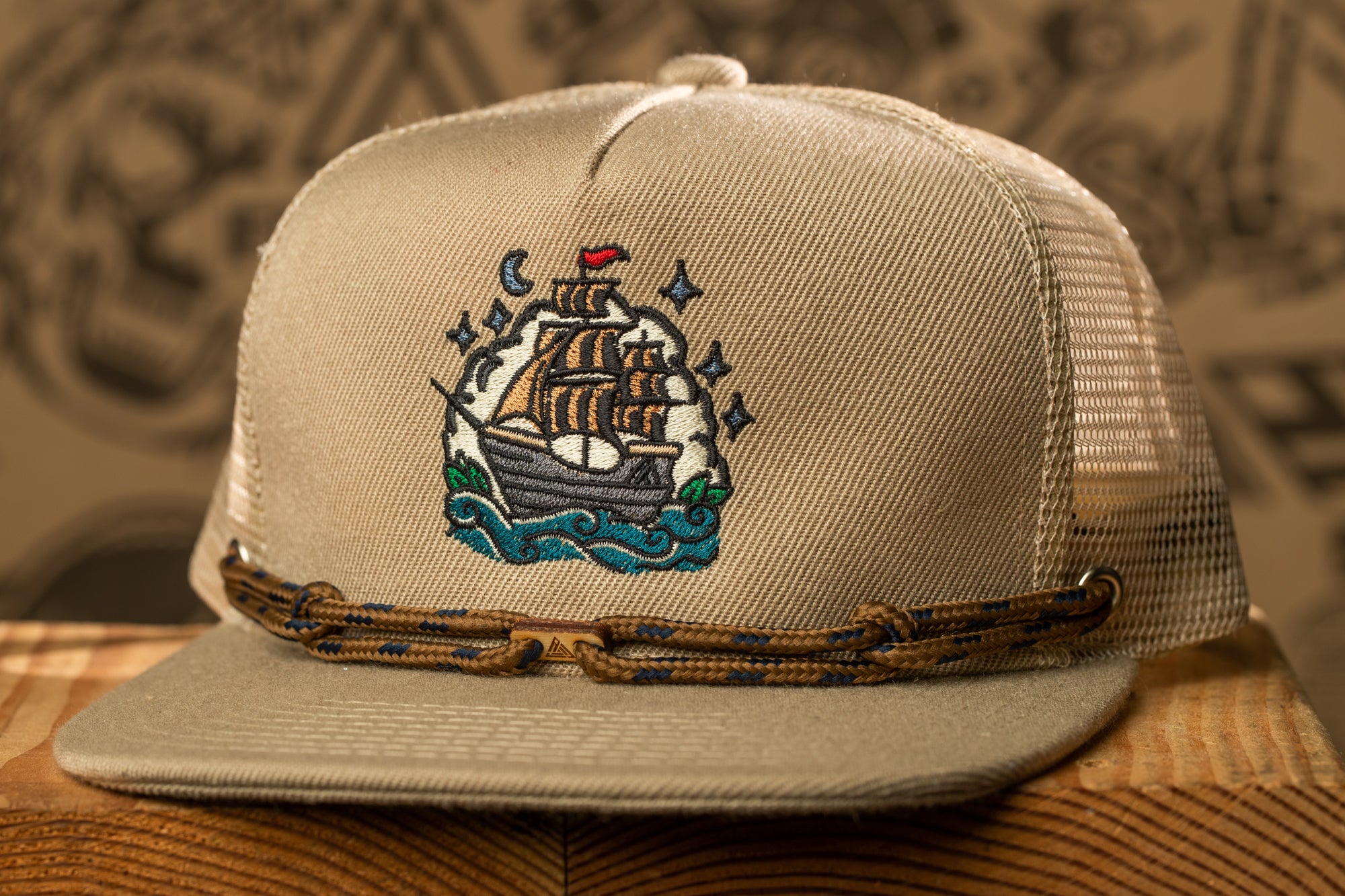 A beige baseball cap with a detailed embroidered design of a ship on the front.