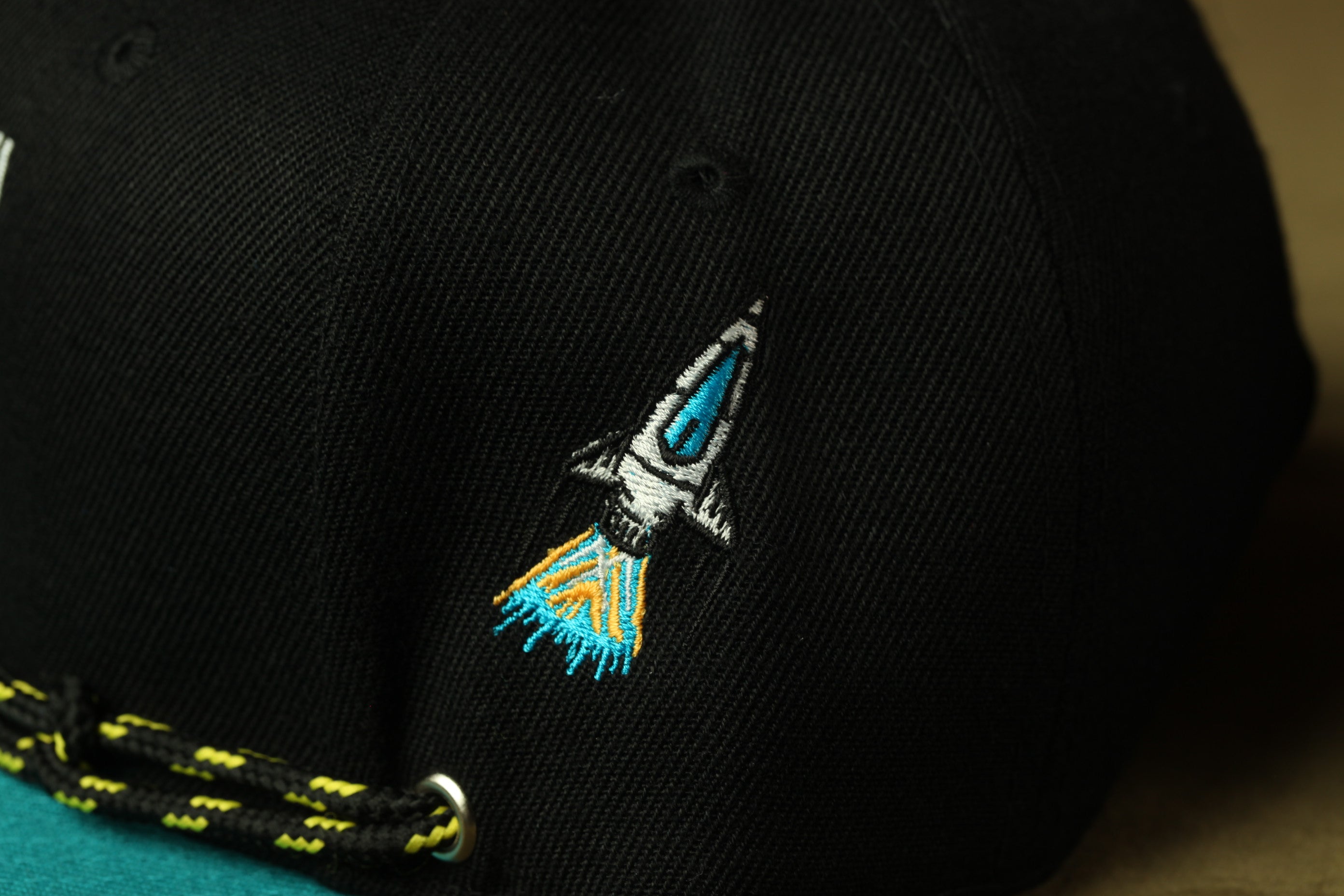 A close-up view of a black baseball cap with a small embroidered rocket ship design on the front.