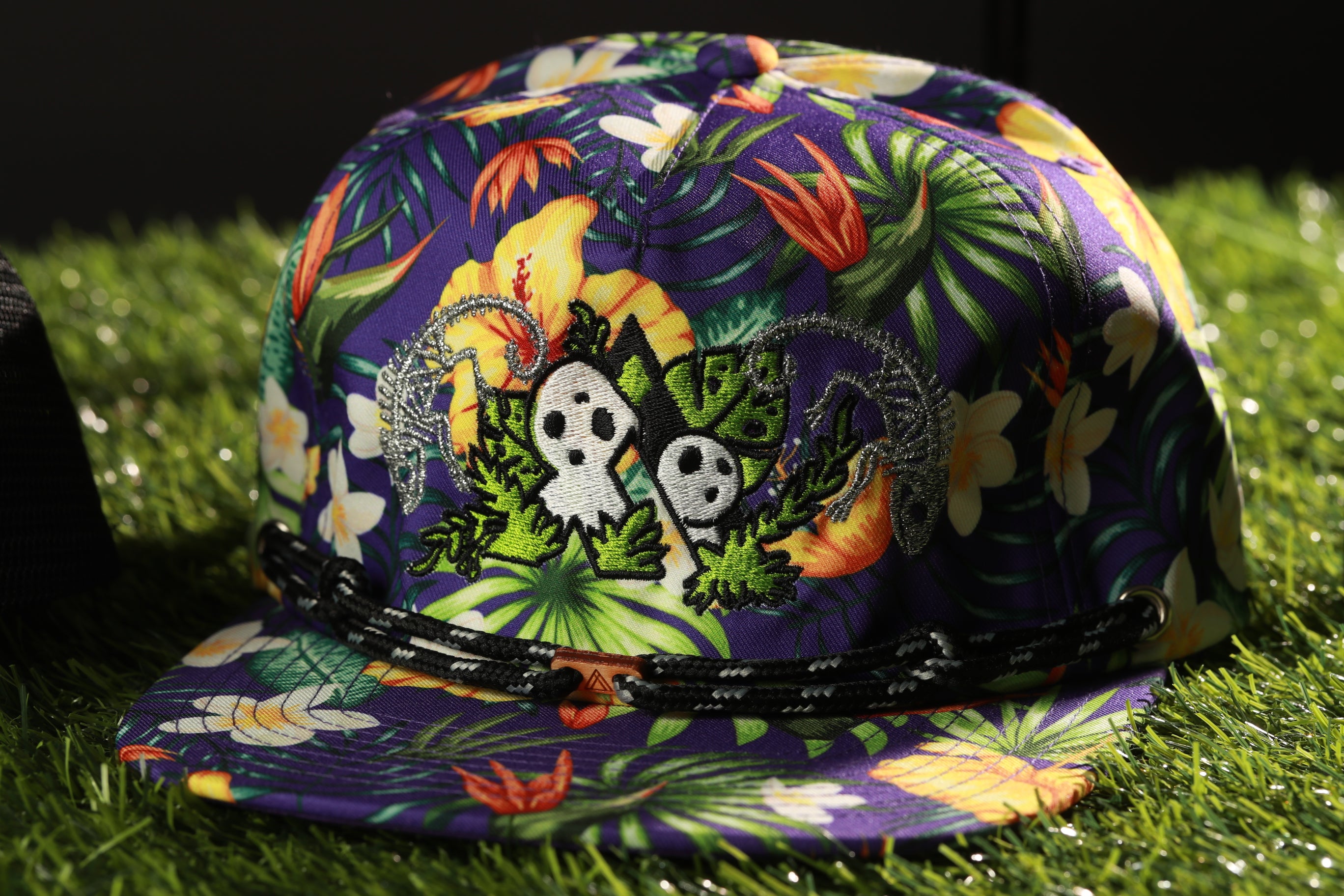 A colorful floral patterned baseball cap with a black strap, resting on a grassy surface.