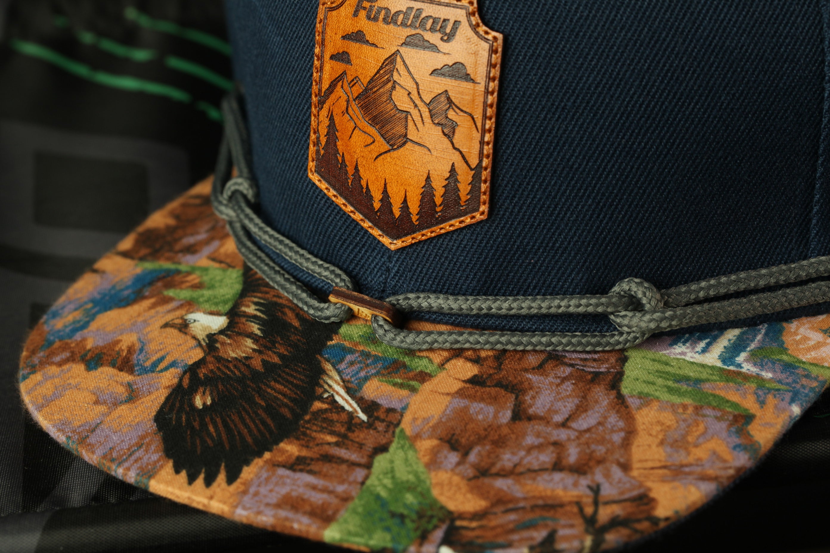 A close-up view of a baseball cap with a detailed embroidered mountain landscape design on the front.