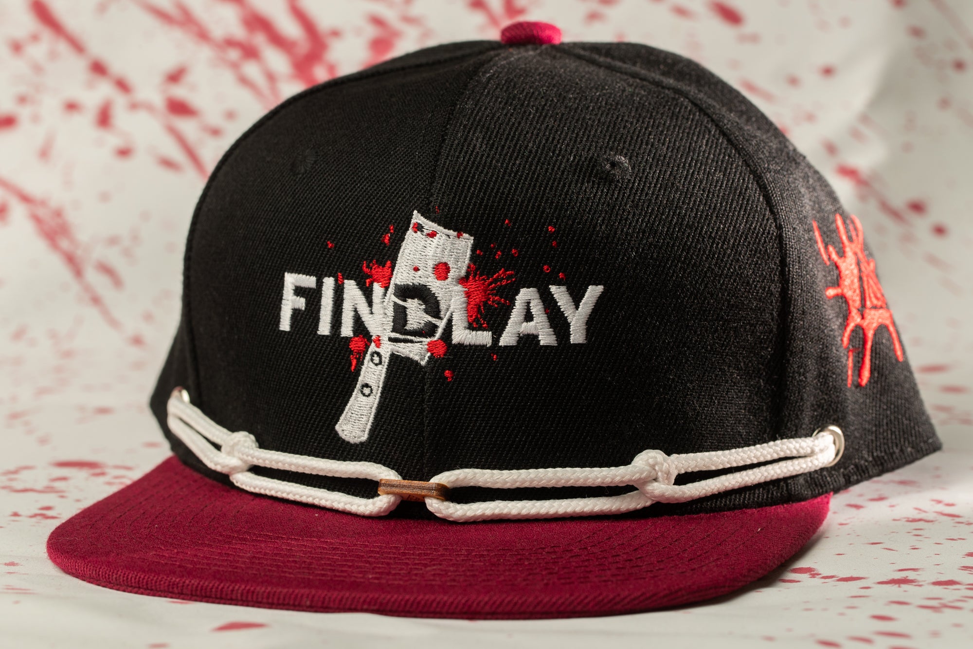 A black baseball cap with a red brim and white text on the front, featuring a graphic of a knife and the word "FINDA" printed on it.