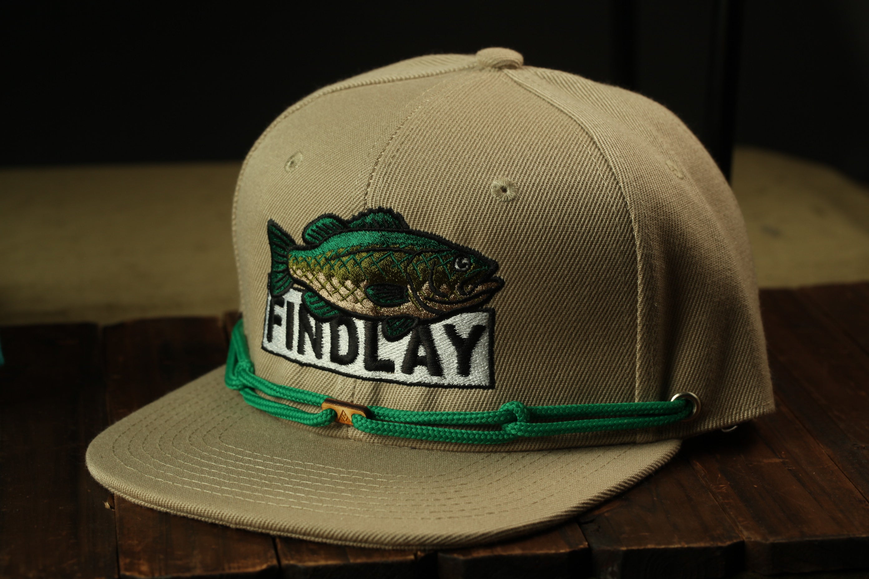 A tan baseball cap with a fish embroidered on it, featuring the word "FINDLAY" on the front.