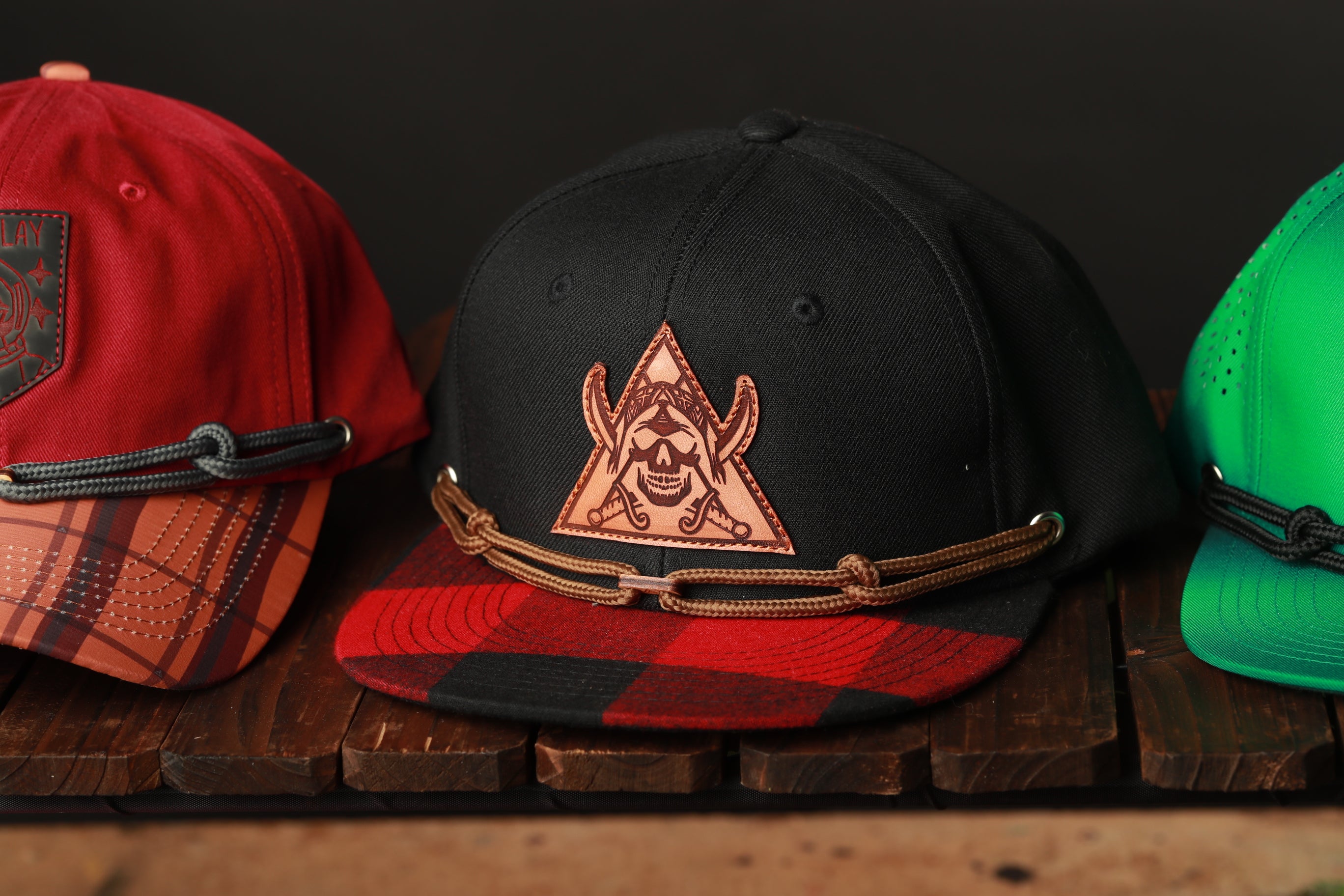 Three baseball caps are displayed on a wooden surface, each with a distinct color and pattern.