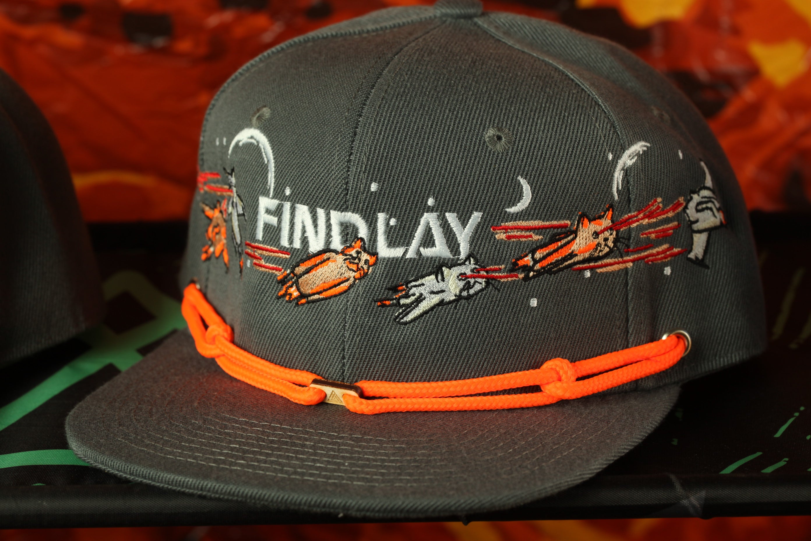 A gray baseball cap with orange straps and various cartoon-like designs on the front.