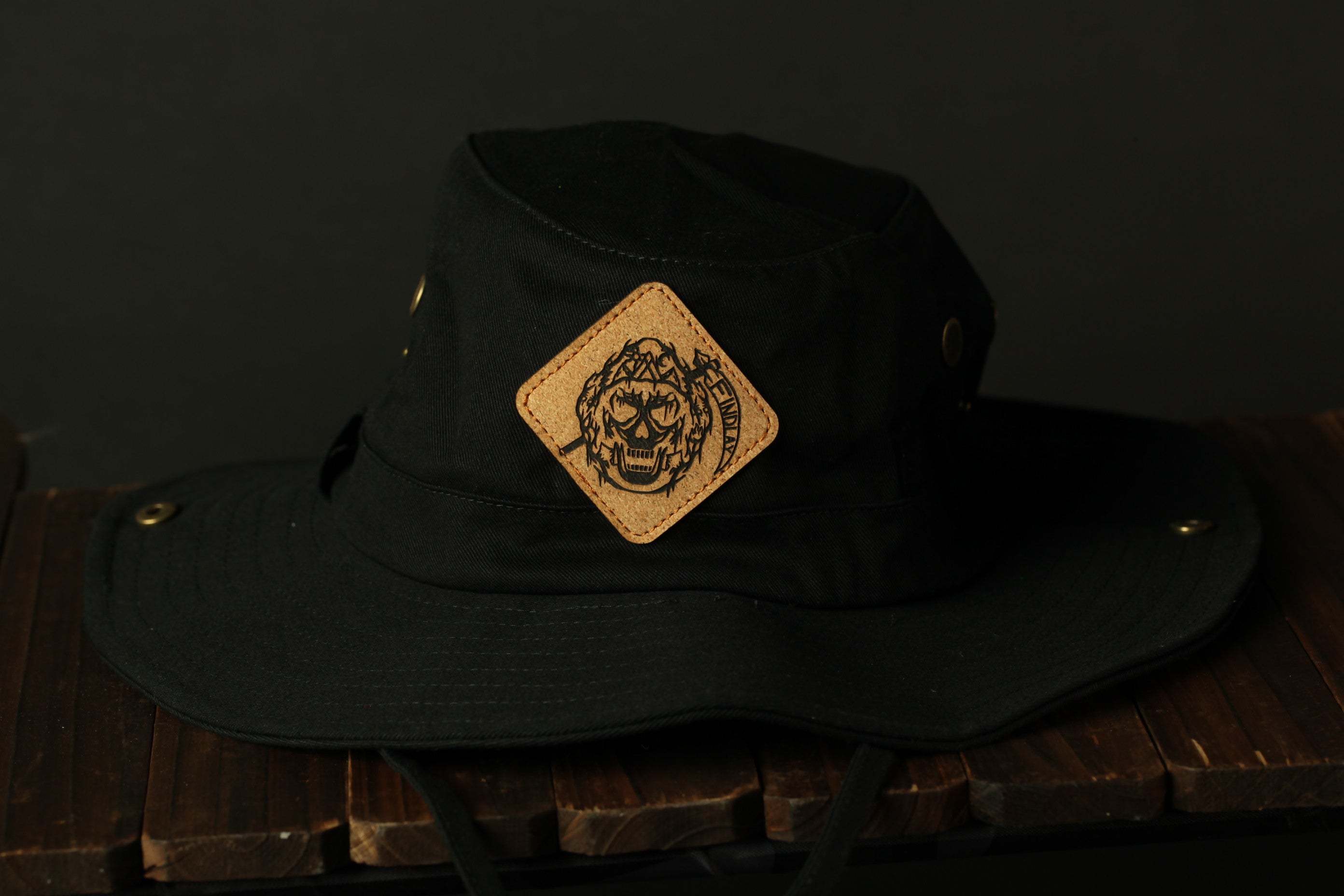 A black bucket hat with a skull patch on the front, placed on a wooden surface.