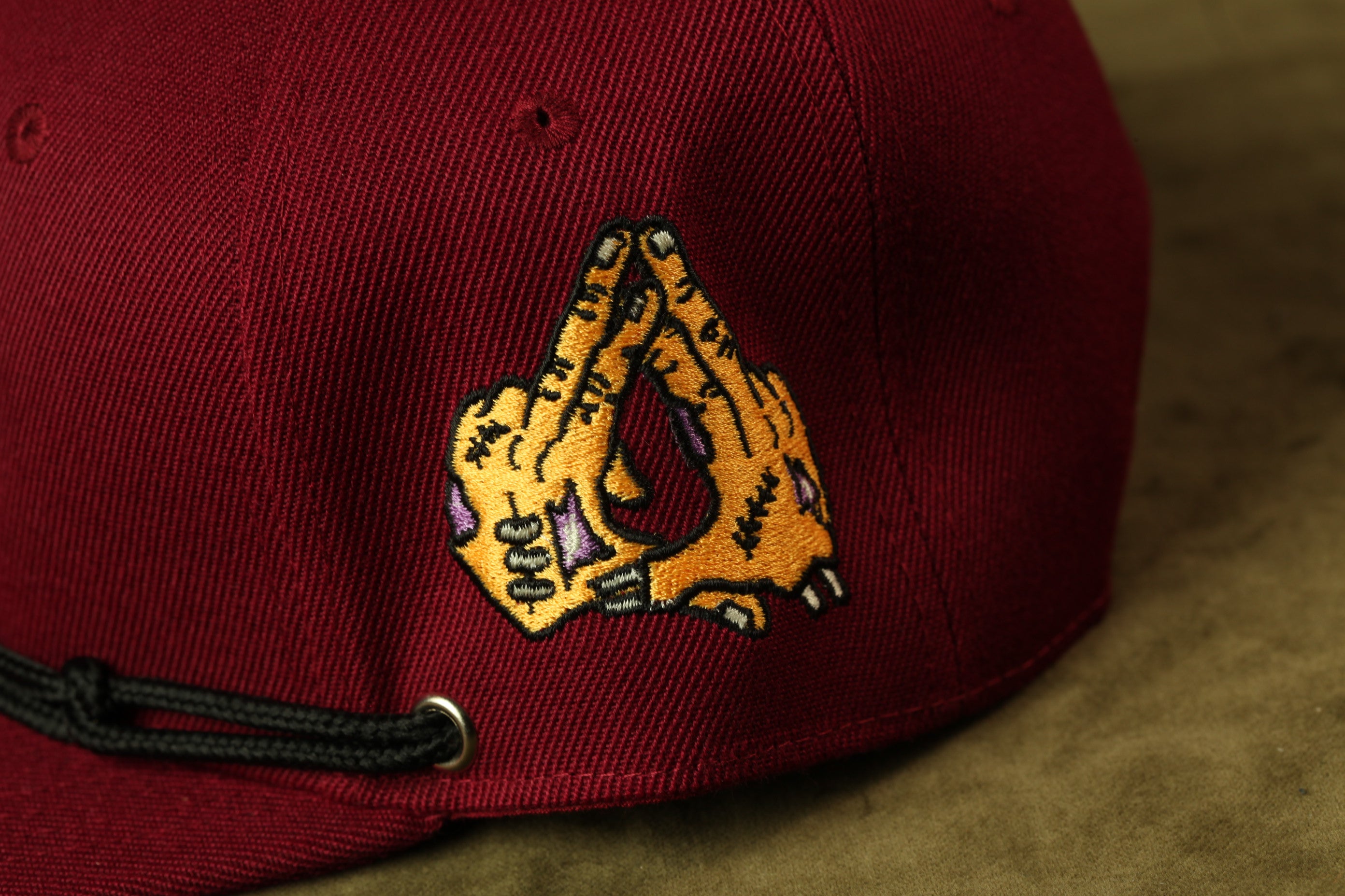 A close-up view of a burgundy baseball cap with a unique embroidered design on the front.