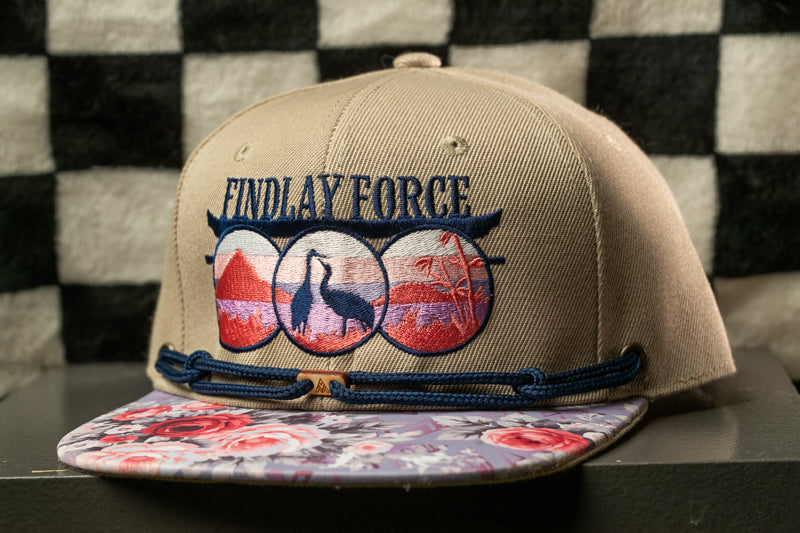A beige baseball cap with a floral pattern and the text "FINDLAY FORCE" printed on it, sitting on a surface with a black and white checkered pattern.