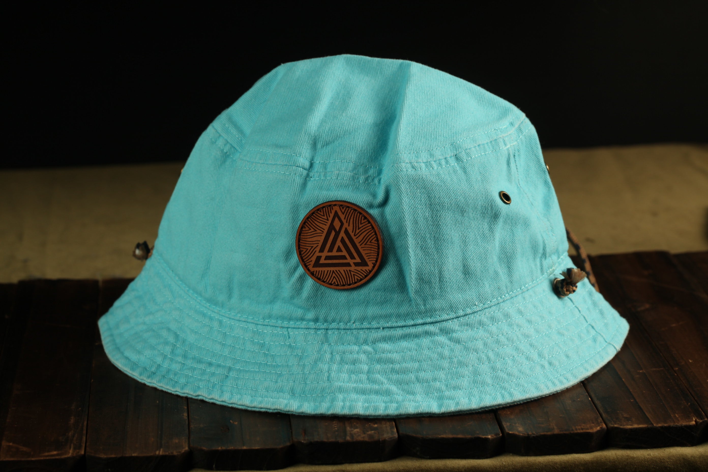 A turquoise bucket hat with a leather patch on the front, placed on a wooden surface.