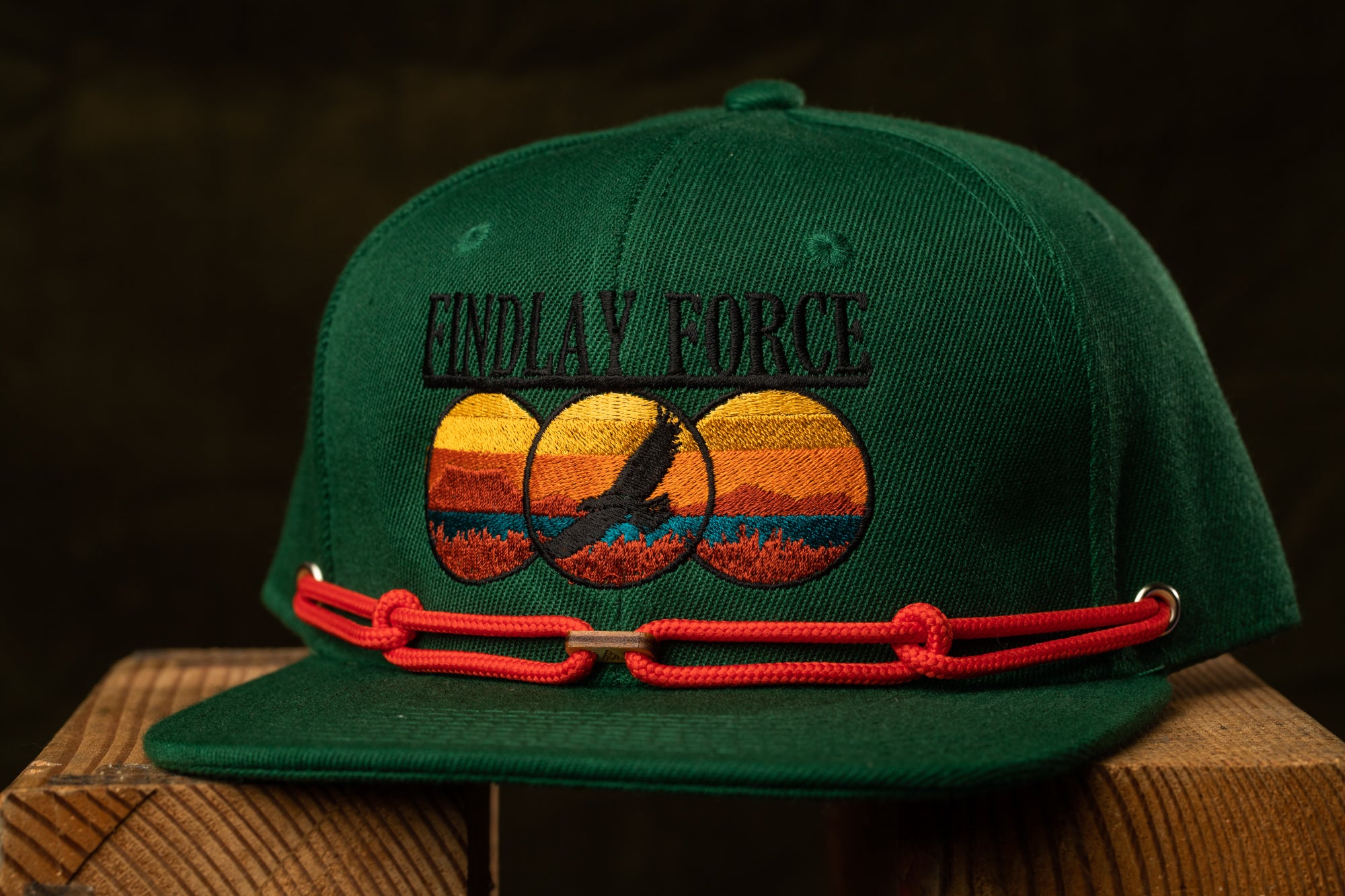 A green baseball cap with a red string and a graphic design on the front.