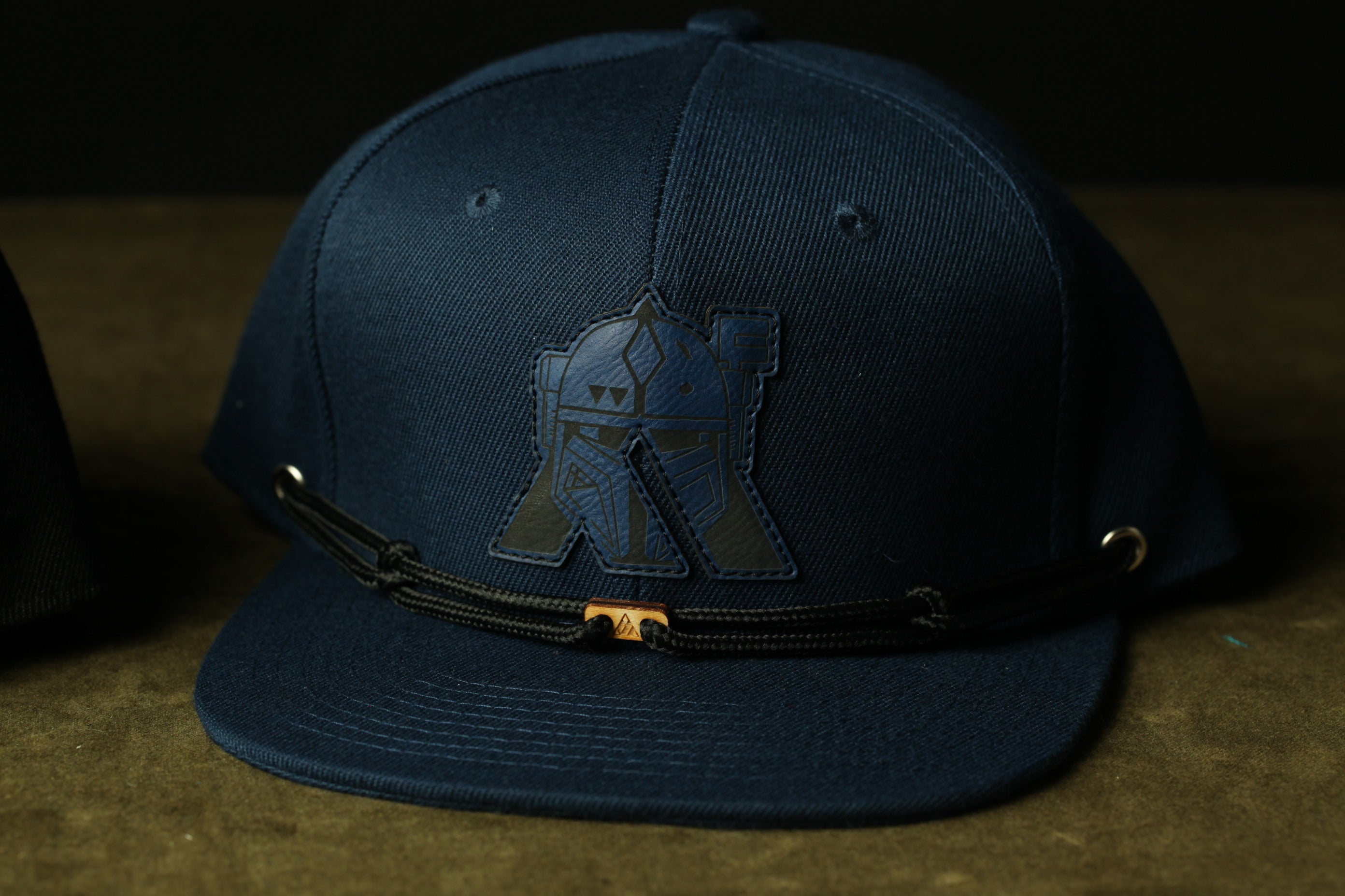 A navy blue baseball cap with a black strap and a unique logo on the front.
