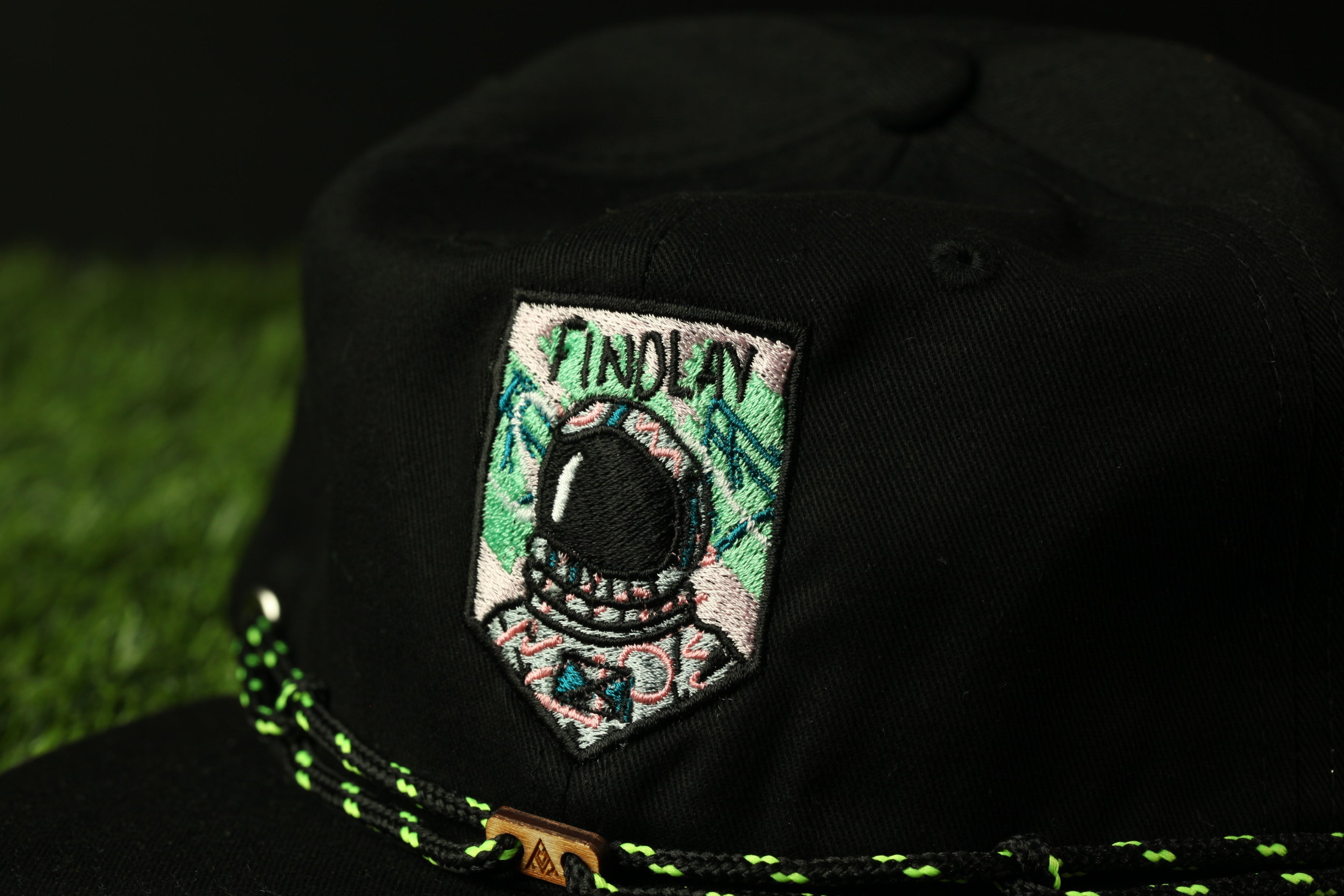 A close-up view of a black baseball cap with a colorful patch on the front, featuring a helmet and the word "FINOLAY" written on it.