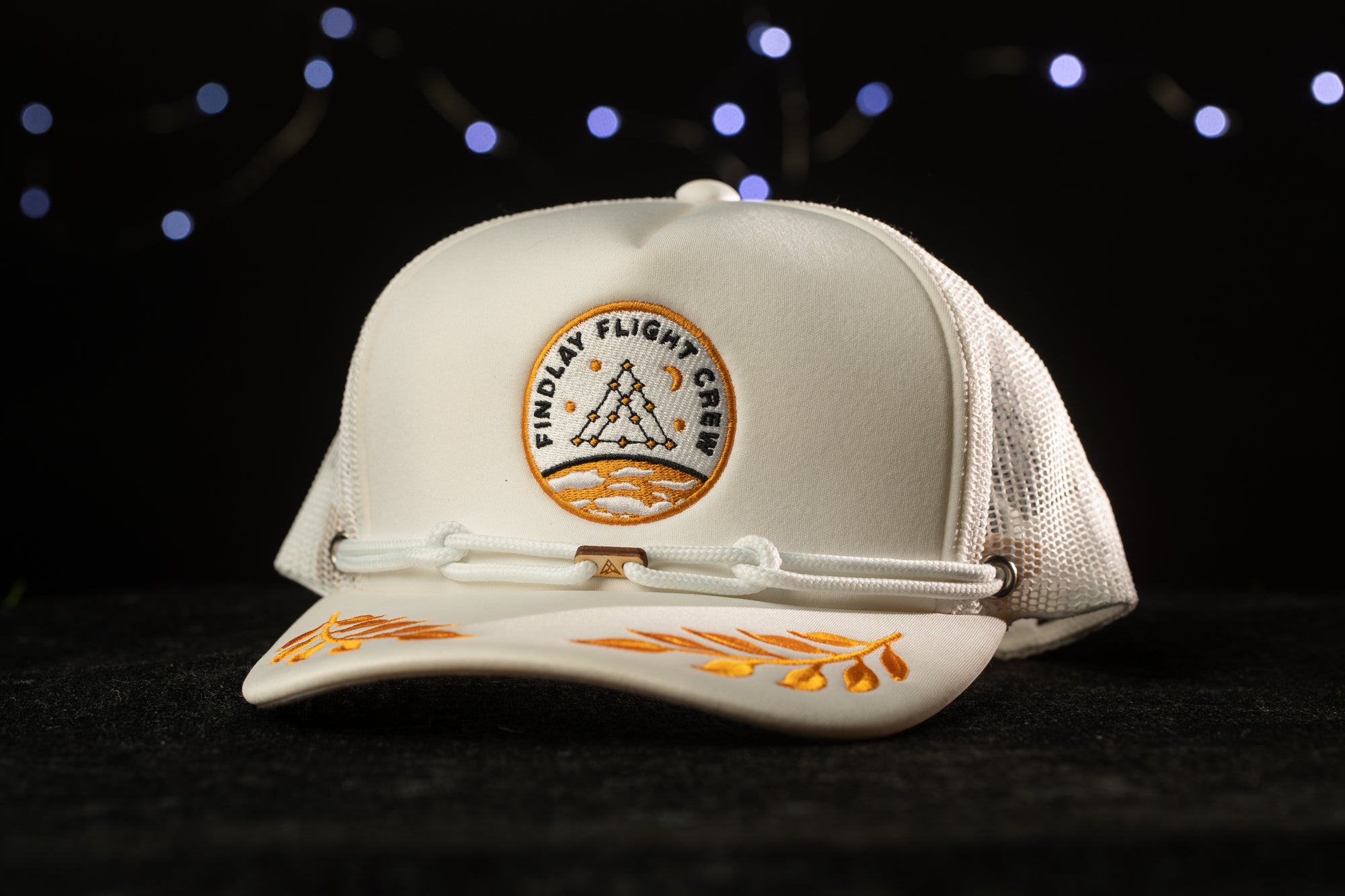A white baseball cap with a logo on it, placed on a black surface against a background of blue lights.