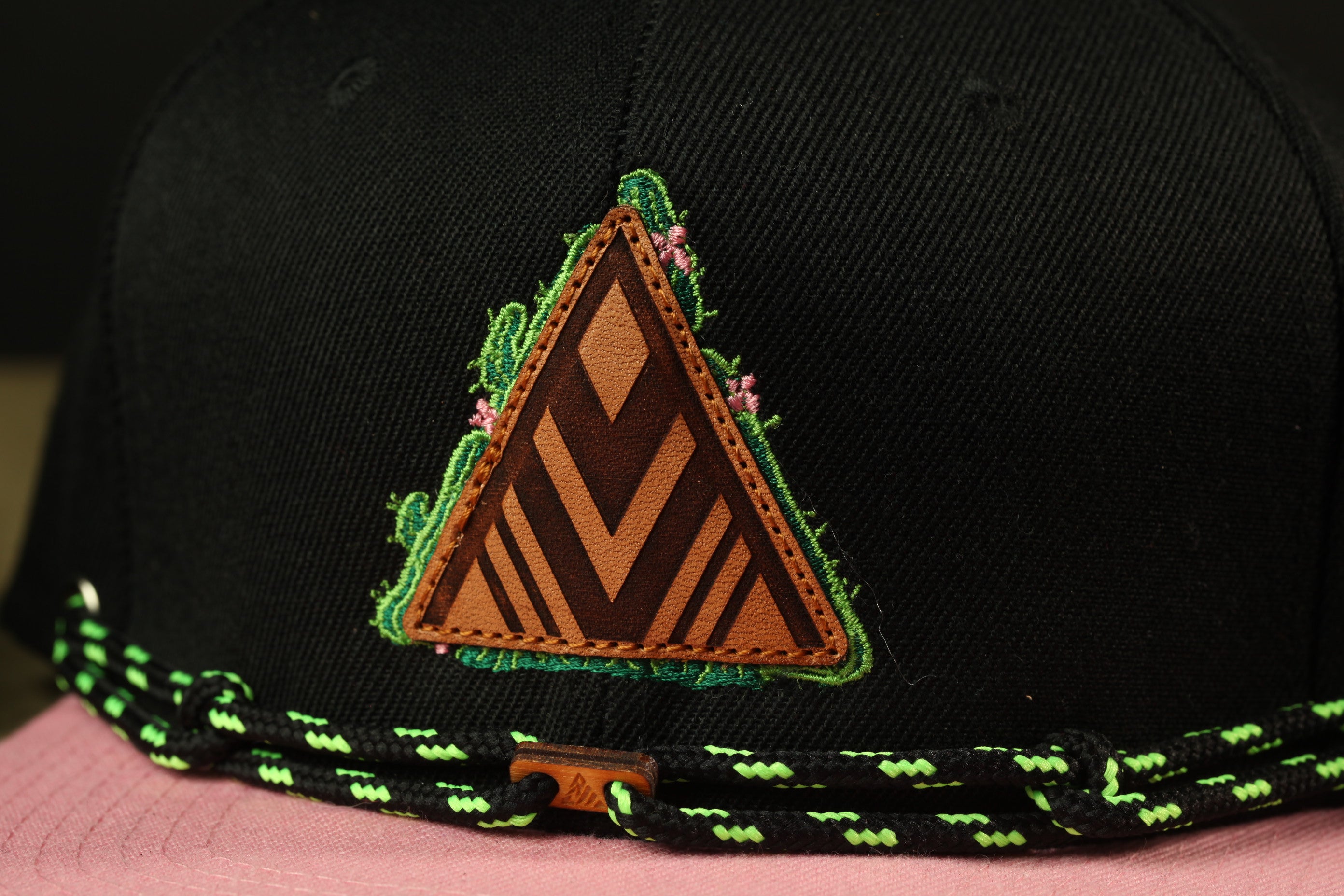 A close-up view of a black baseball cap with a triangular patch featuring a floral design and a brown leather-like texture.
