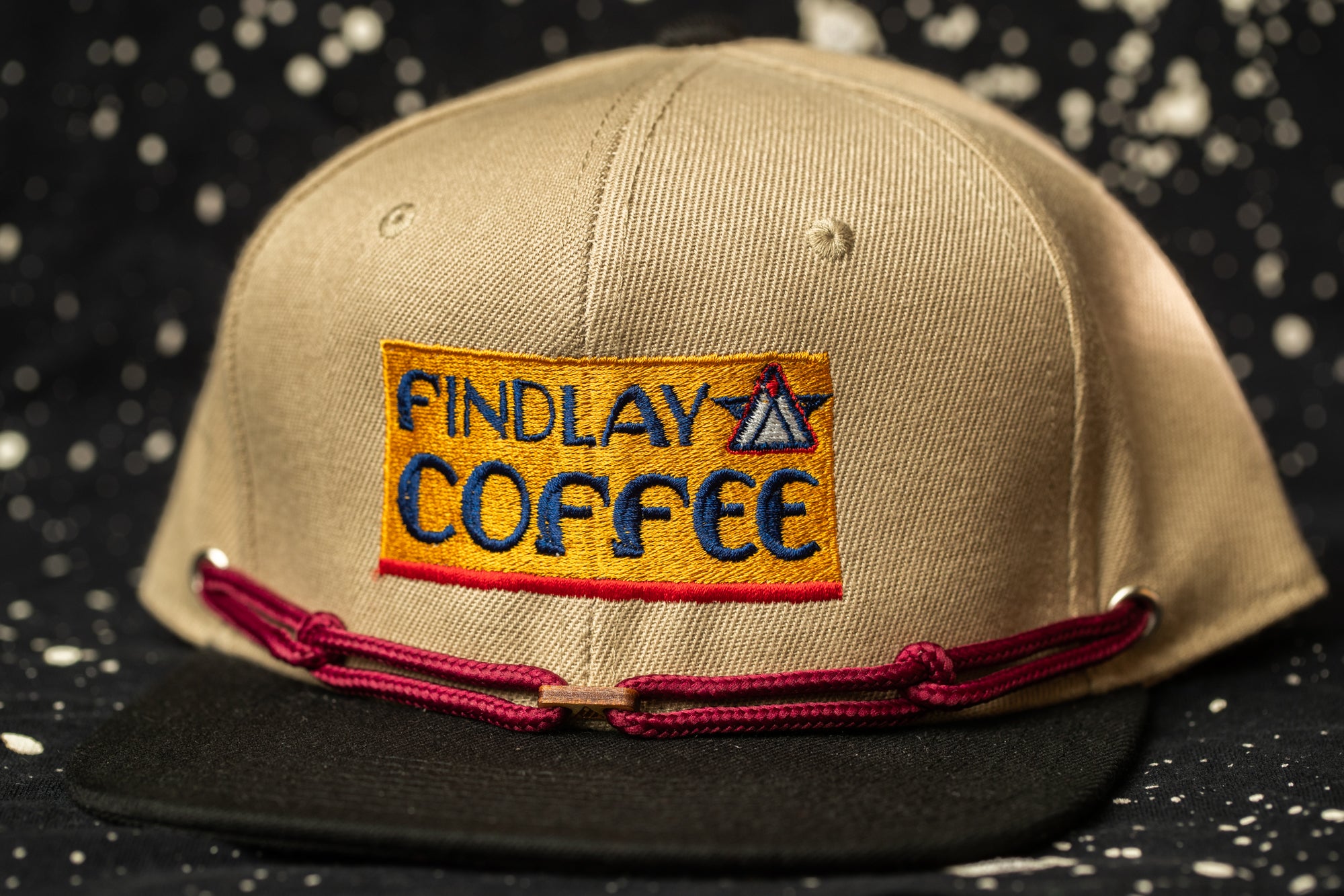 A beige baseball cap with a red string and a patch on the front that says "Findlay Coffee".